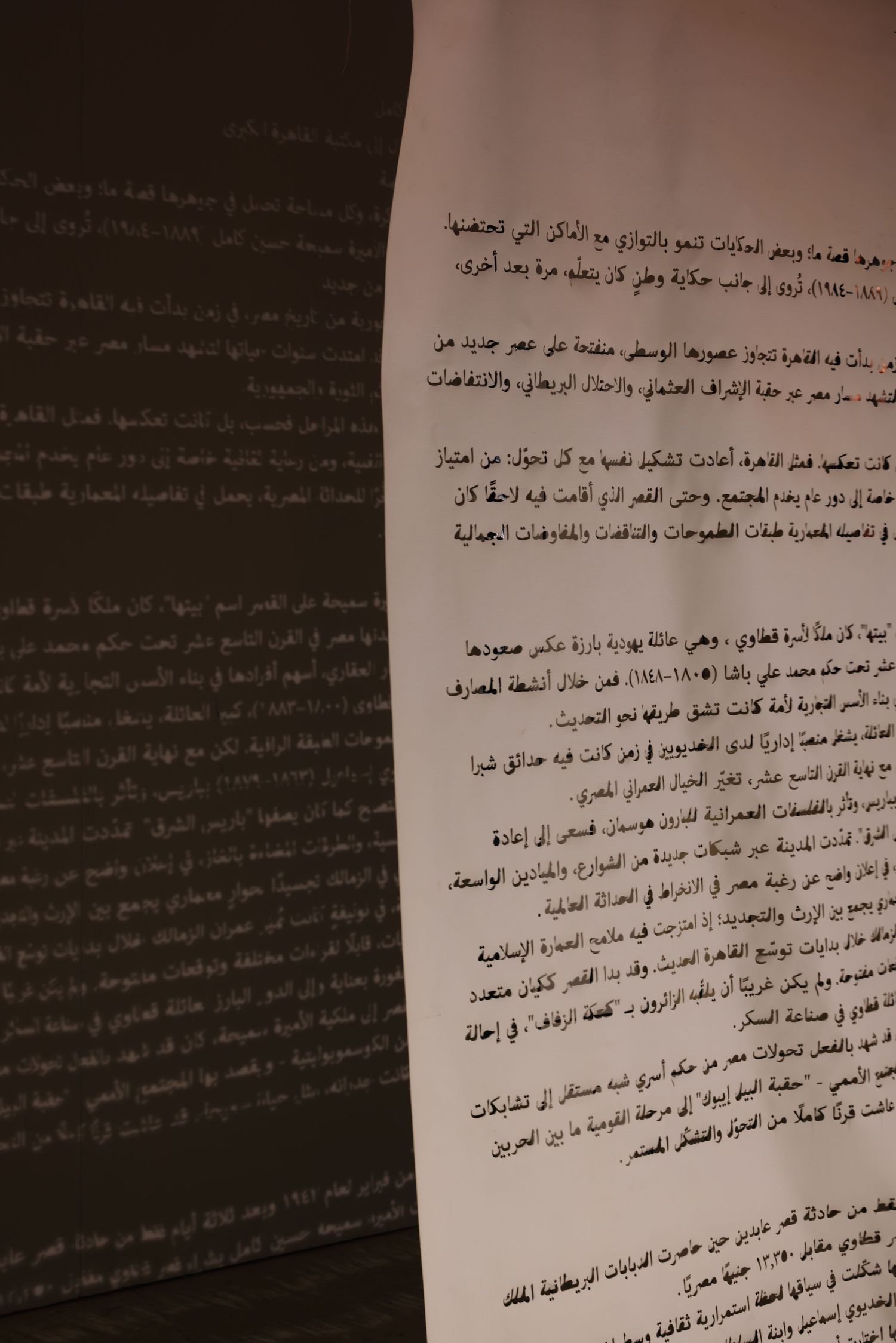 Close-up of Arabic text document with projected Arabic script visible on dark wall in background.