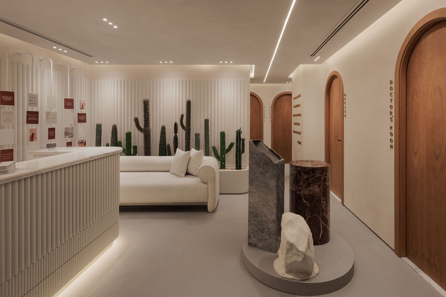 Bright minimalist showroom with cactus wall art, cream sofa, marble sculptures on a pedestal, and arched wooden doorways.