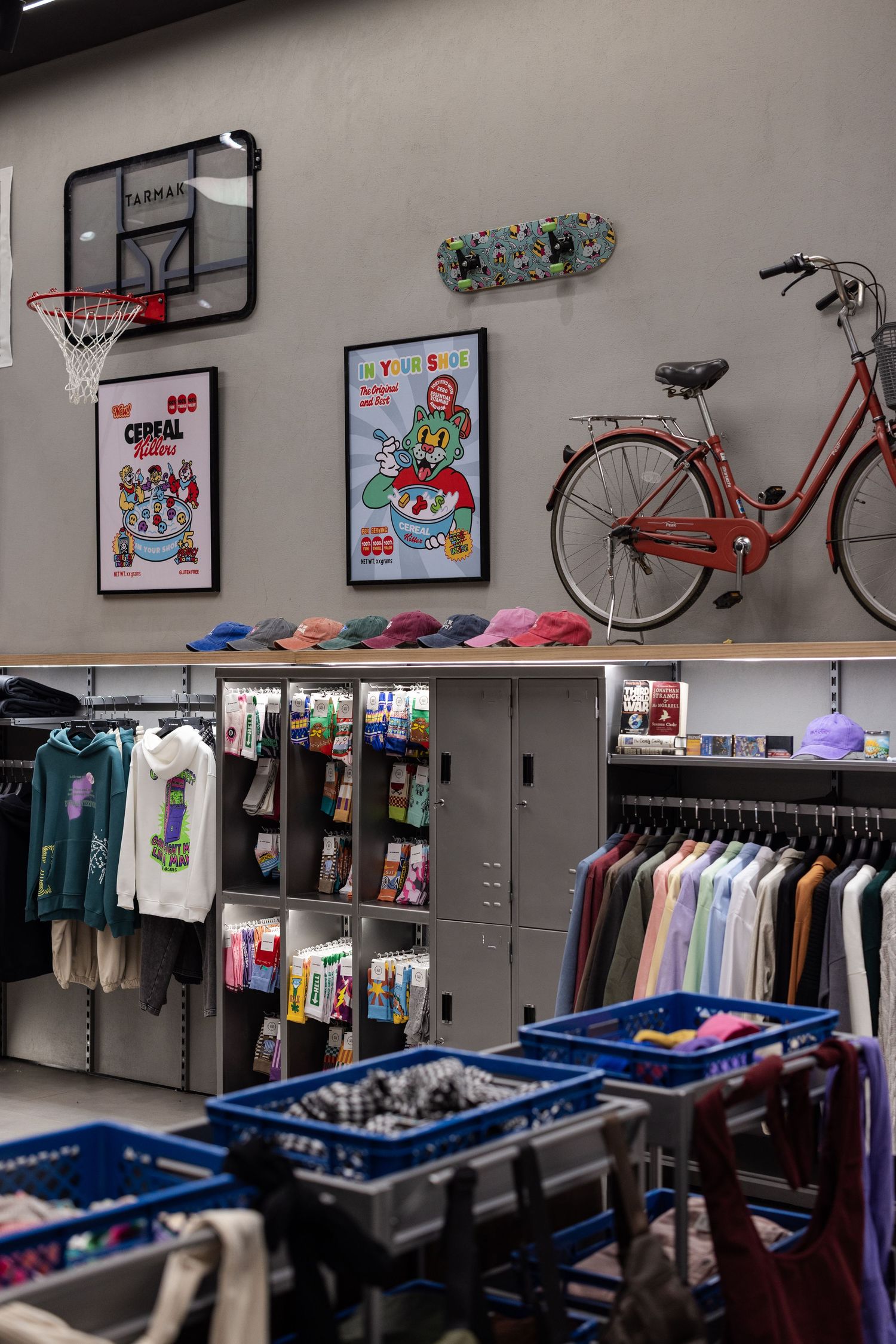 Eclectic retail store wall display with basketball hoop, skateboard, bicycle, posters, hats, and clothing racks.