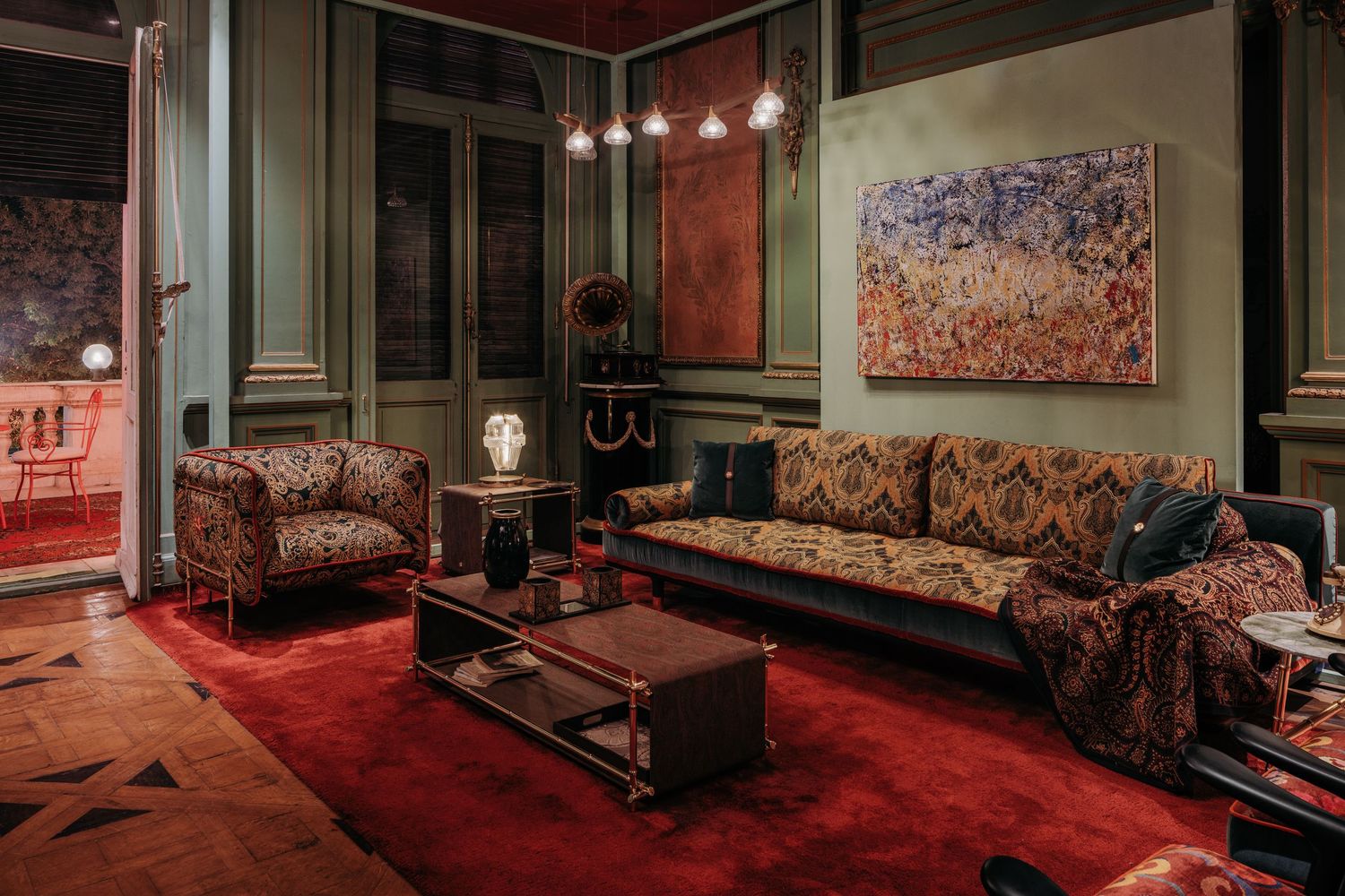 Luxurious eclectic living room with patterned sofas, red carpet, green walls, and abstract artwork in moody lighting.