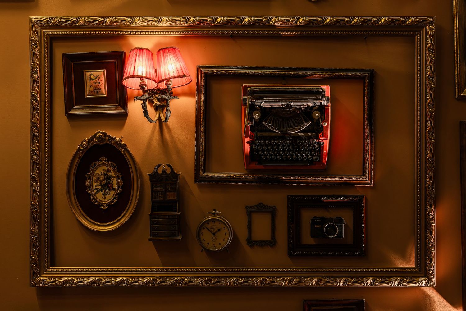 Decorative wall display with ornate frames, vintage typewriter, antique clock, and wall sconce lamp.