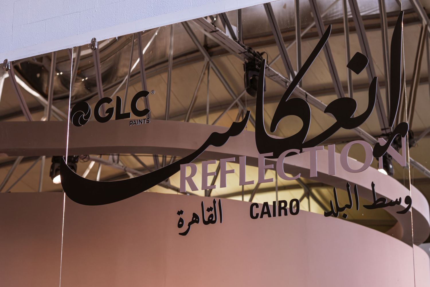 GLC Paints Reflections Cairo exhibition sign with Arabic calligraphy hanging from ceiling structure.