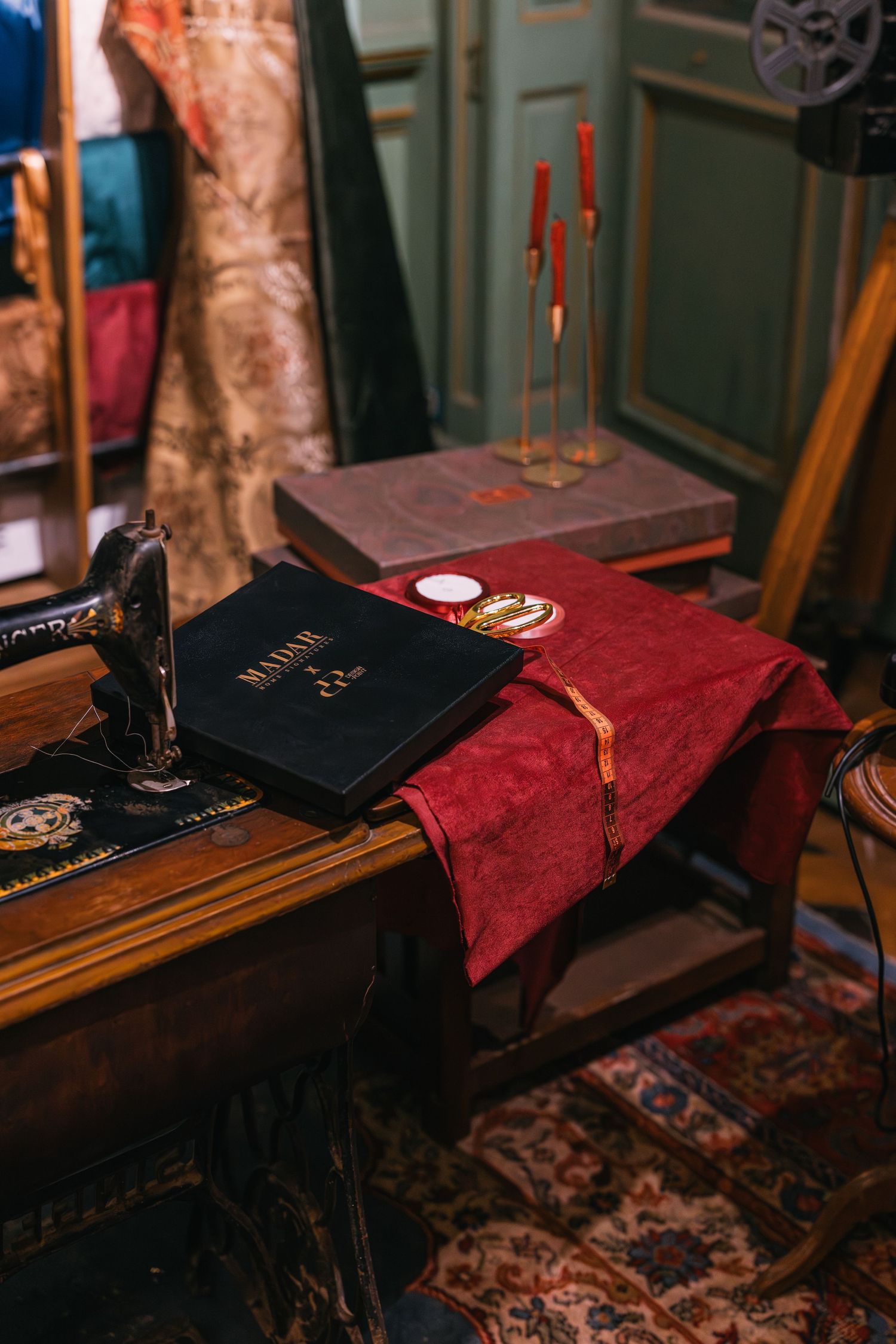 Vintage sewing machine beside red velvet fabric and black book on wooden table in antique room.
