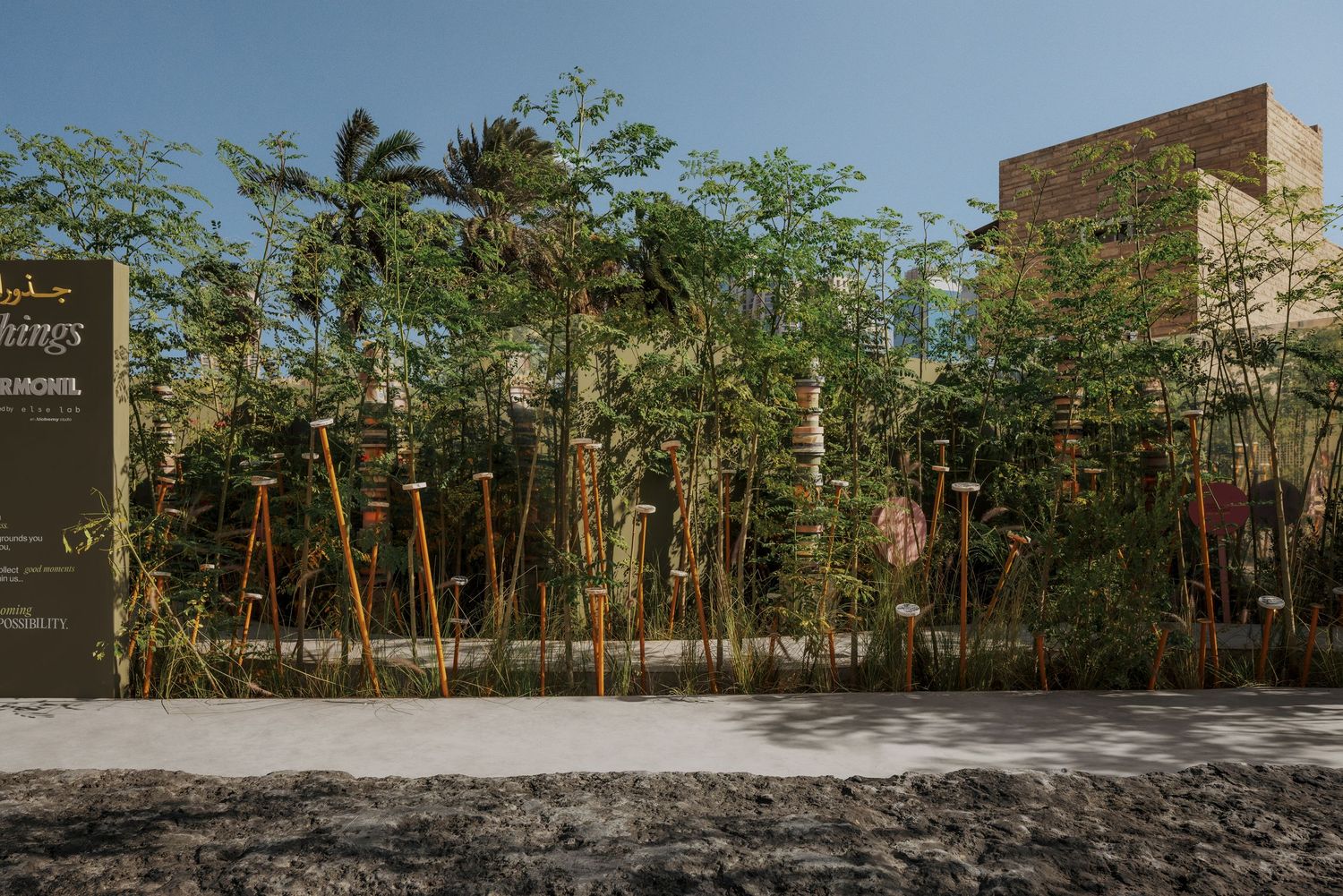Lush garden installation with bamboo poles and tropical trees outside a building with a dark signboard.