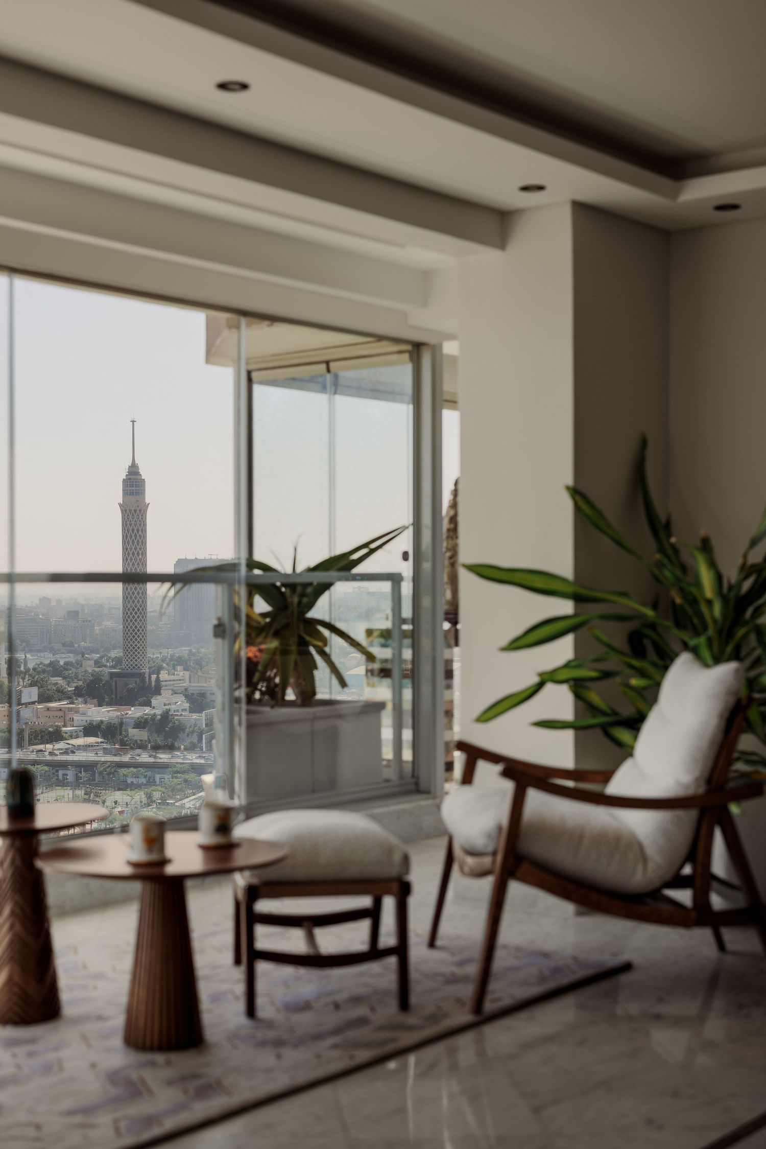 Sophisticated apartment lounge with Cairo Tower view, wooden armchair, white cushions, and elegant side tables.
