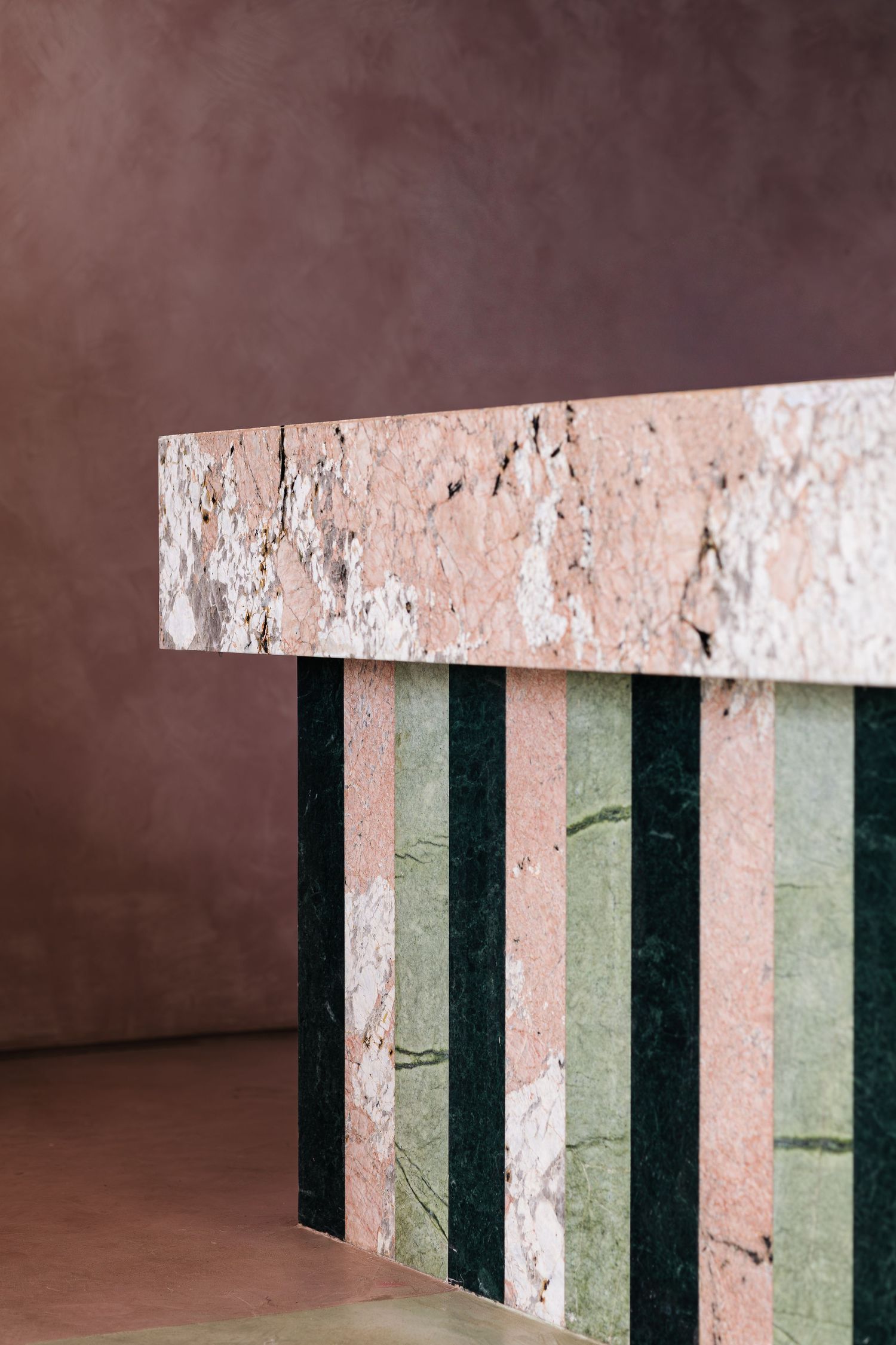 Close-up of pink travertine marble reception desk with alternating dark green and light marble striped base panels.