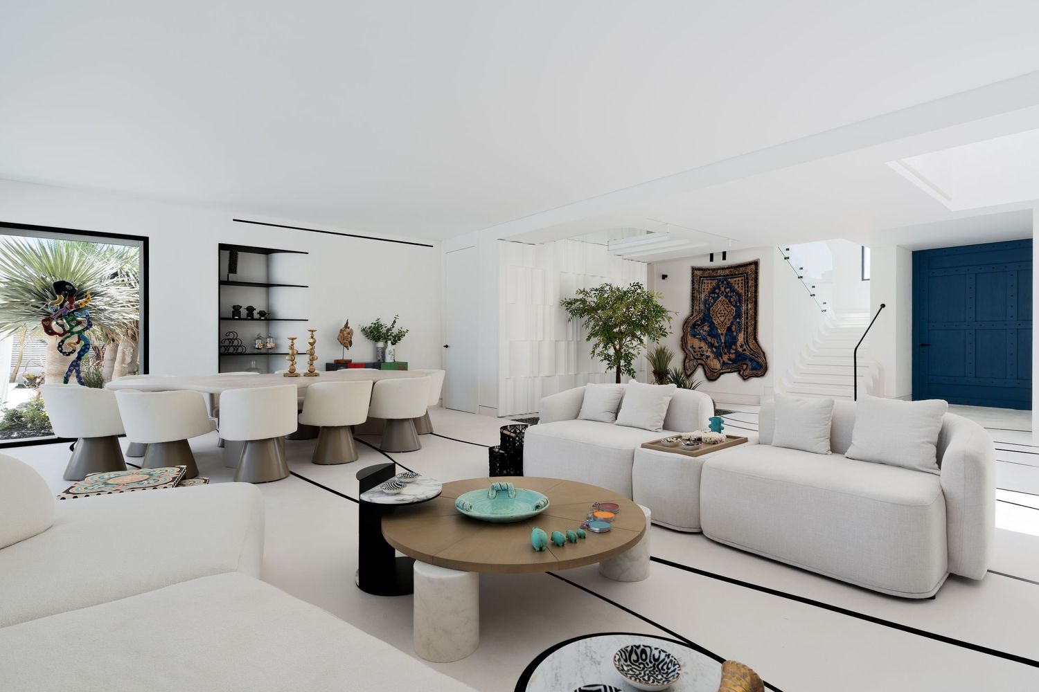 Open-plan white living room with modular sofa, round coffee table, and eclectic art collection.