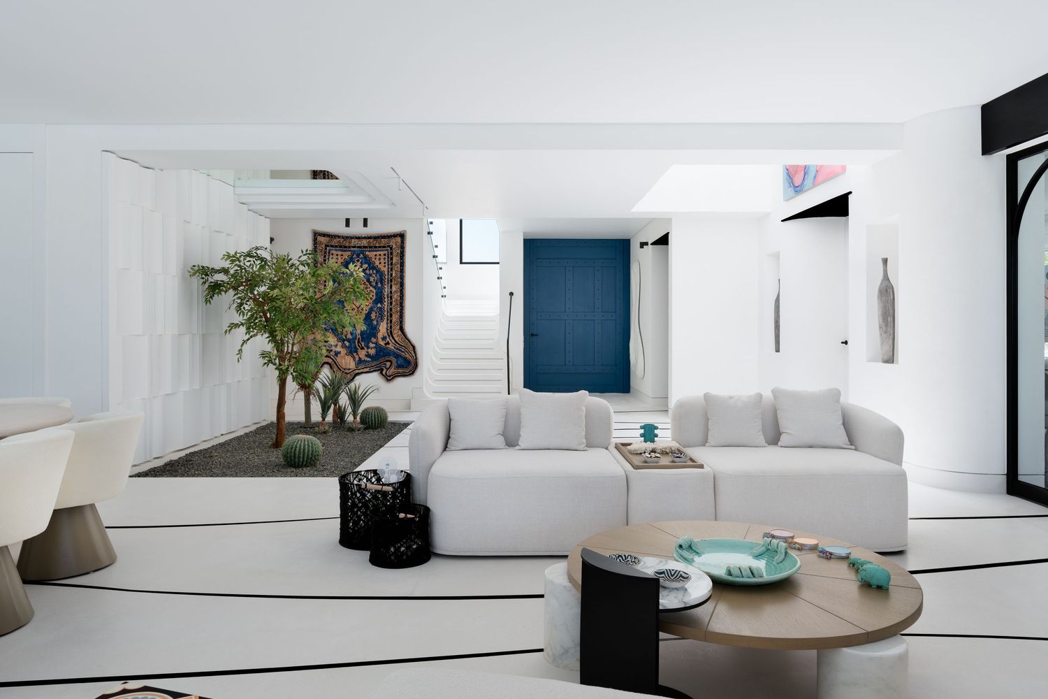 Modern white living room with sectional sofa, round wood coffee table, indoor trees, and blue accent wall.
