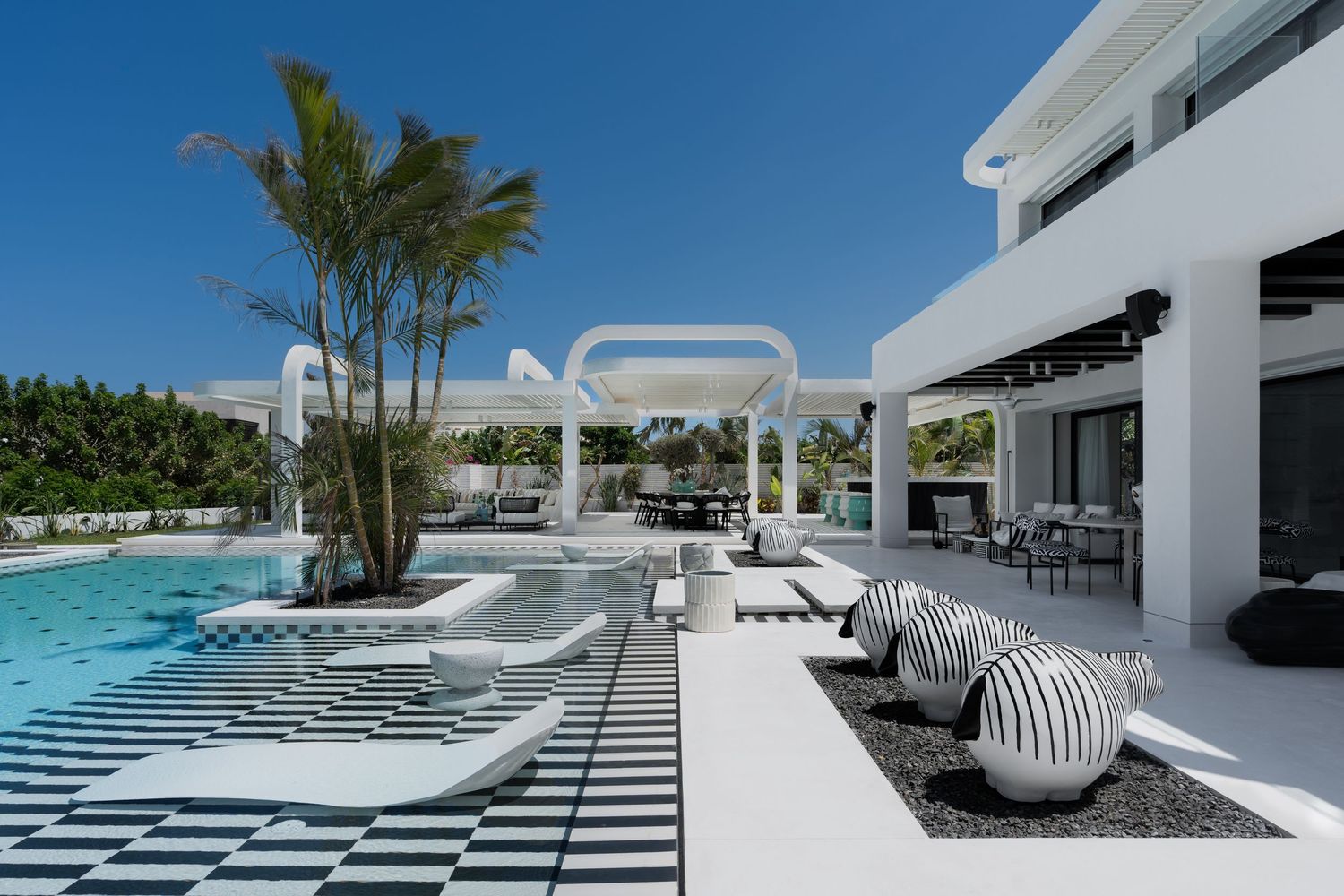Luxury white villa outdoor pool area with black and white checkered deck, palm trees, and modern lounge chairs.