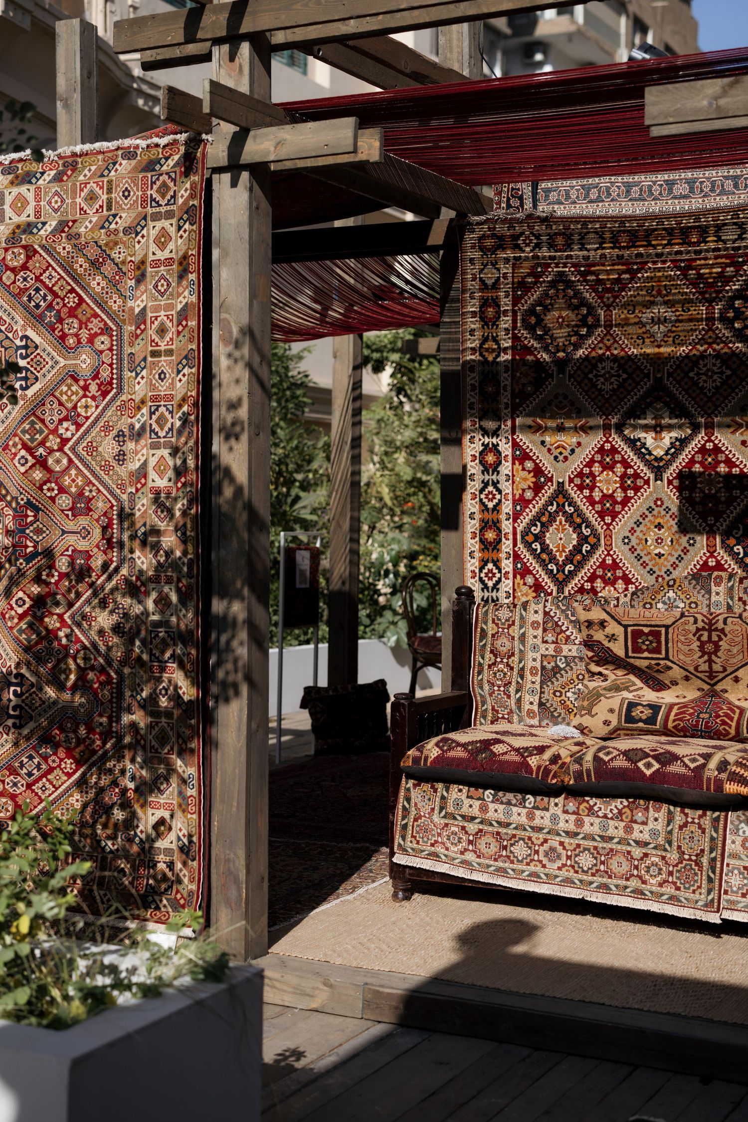 Outdoor seating area adorned with colorful traditional Persian rugs hanging as walls and draped over a sofa.