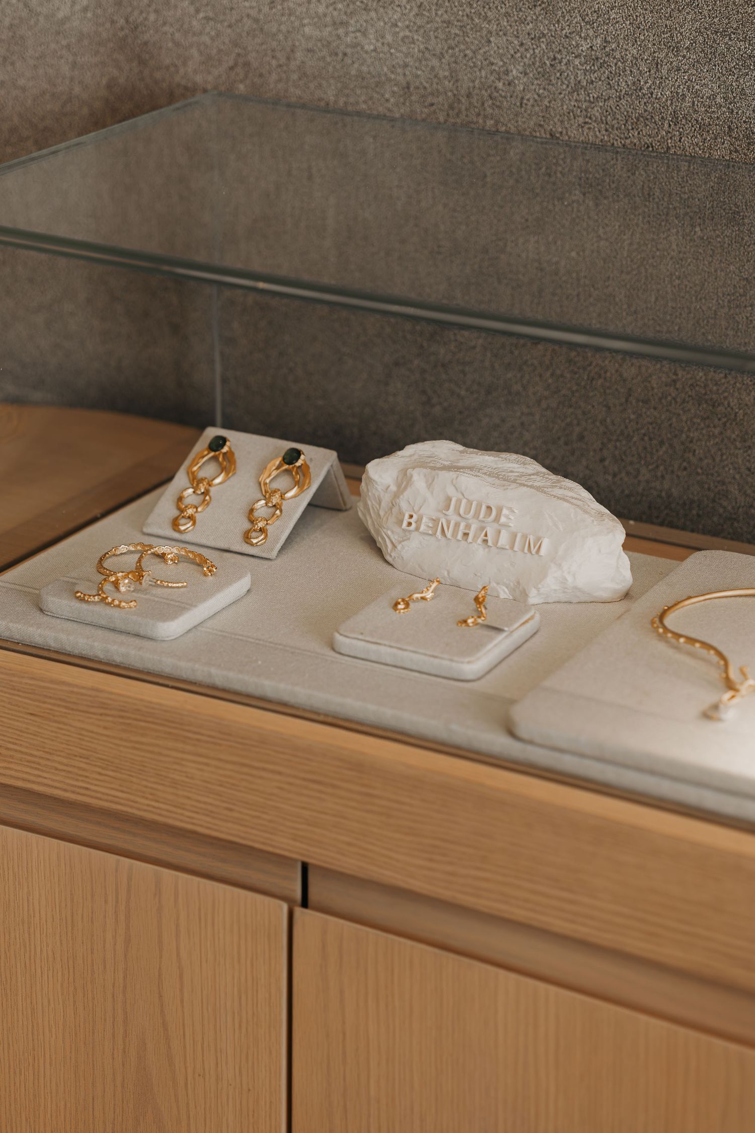 Gold jewelry collection including earrings, rings, and bracelet displayed on white stone props in a glass showcase.