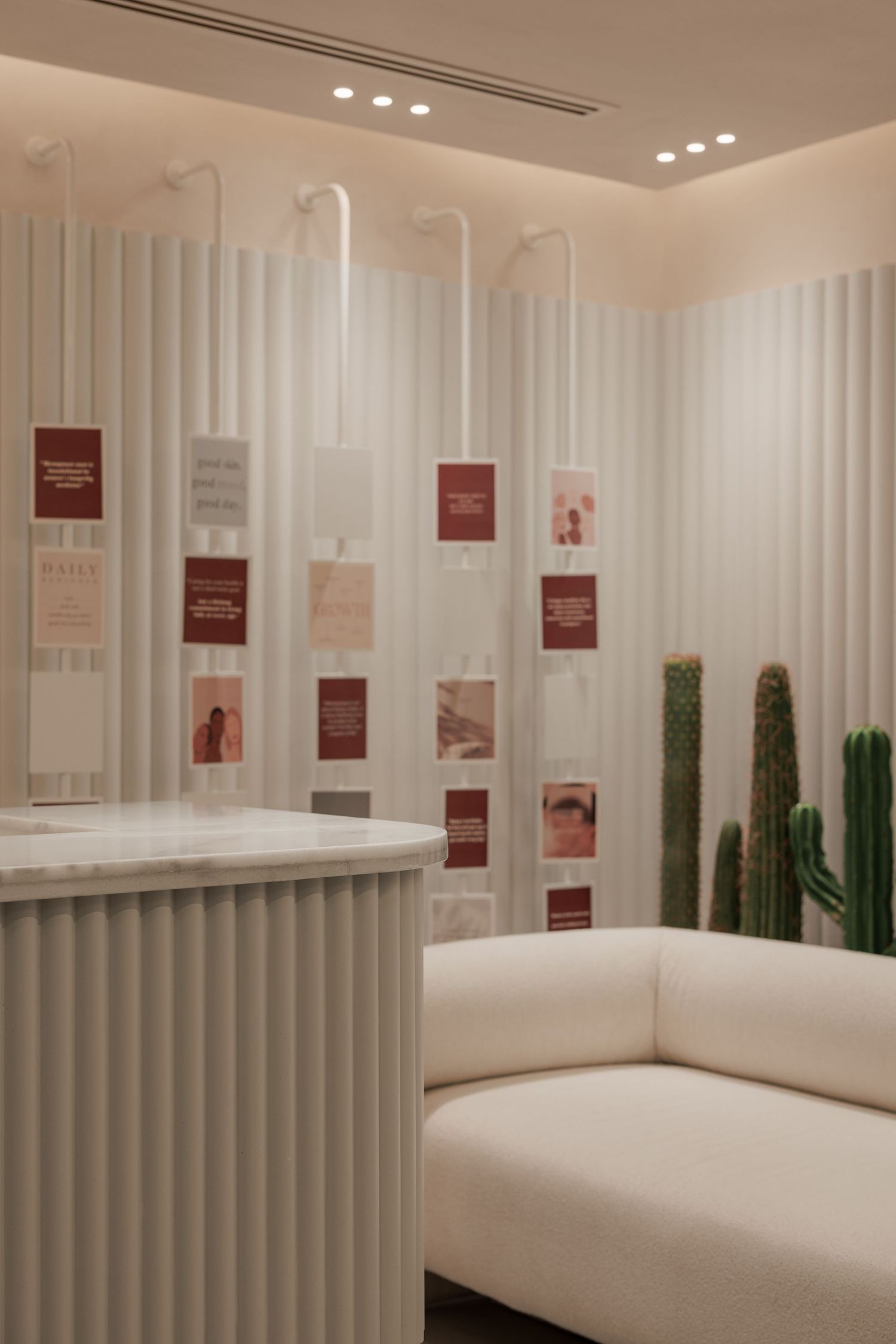 Minimalist white beauty spa reception with fluted walls, cactus plants, cream sofa, and inspirational card displays.