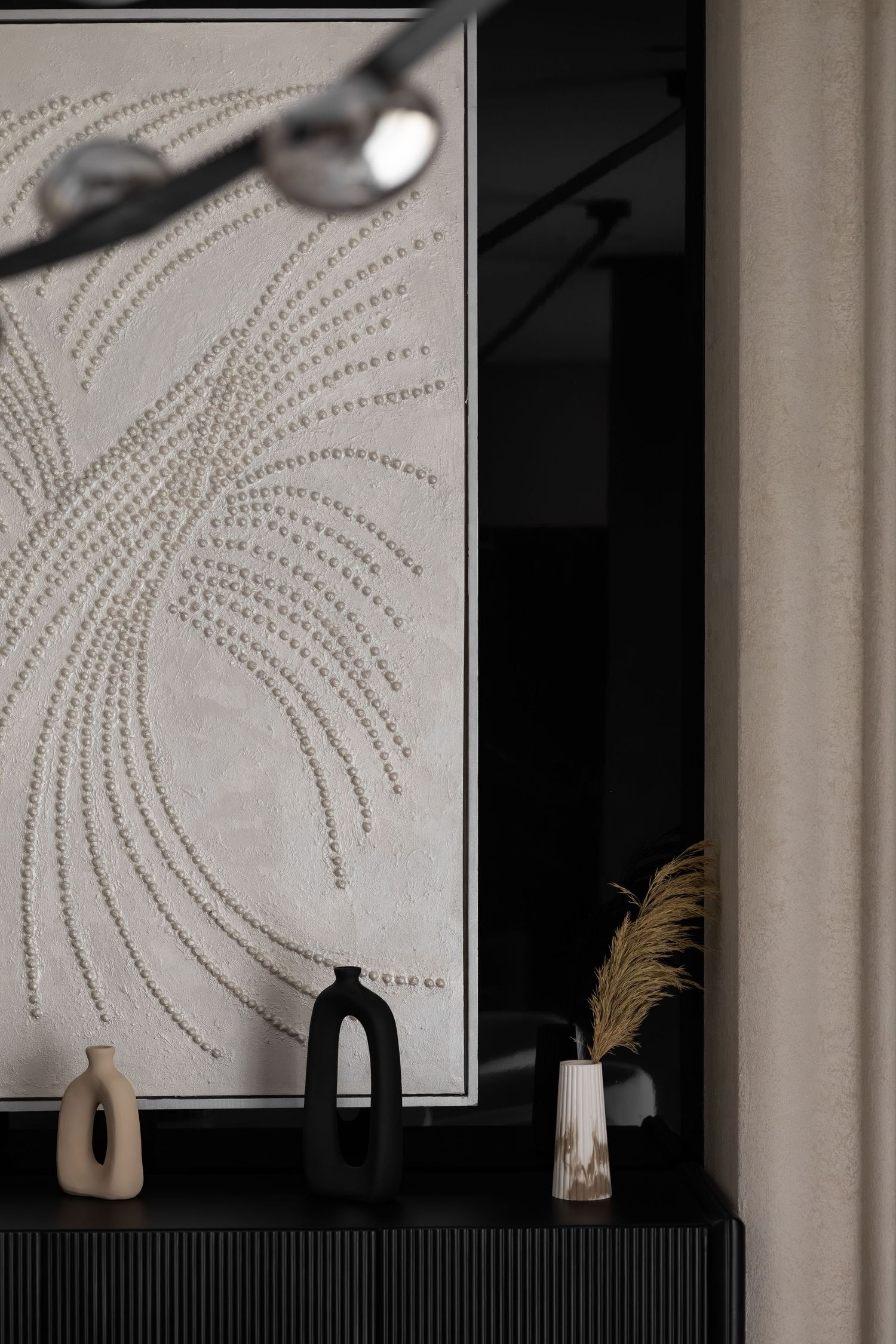 Black sideboard with decorative vases and textured botanical wall art in a modern interior.