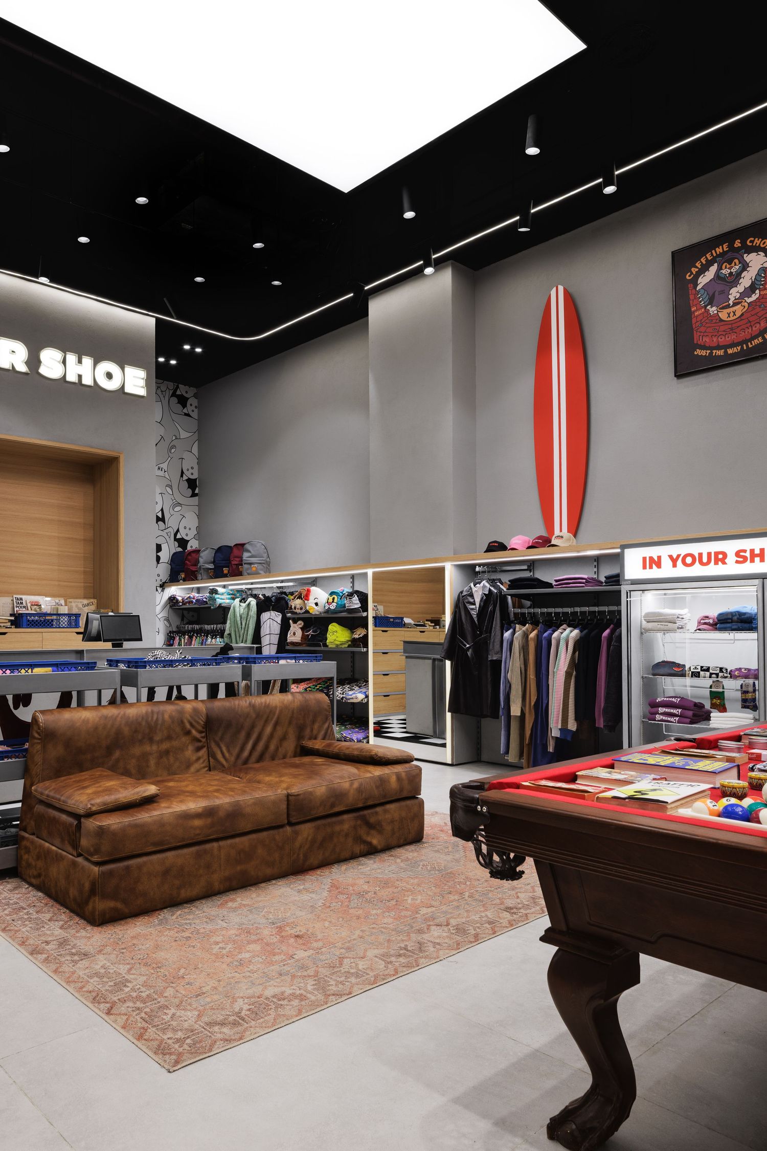 Interior of In Your Shoe retail store featuring a brown leather sofa, pool table, clothing racks, and a red surfboard on the wall.