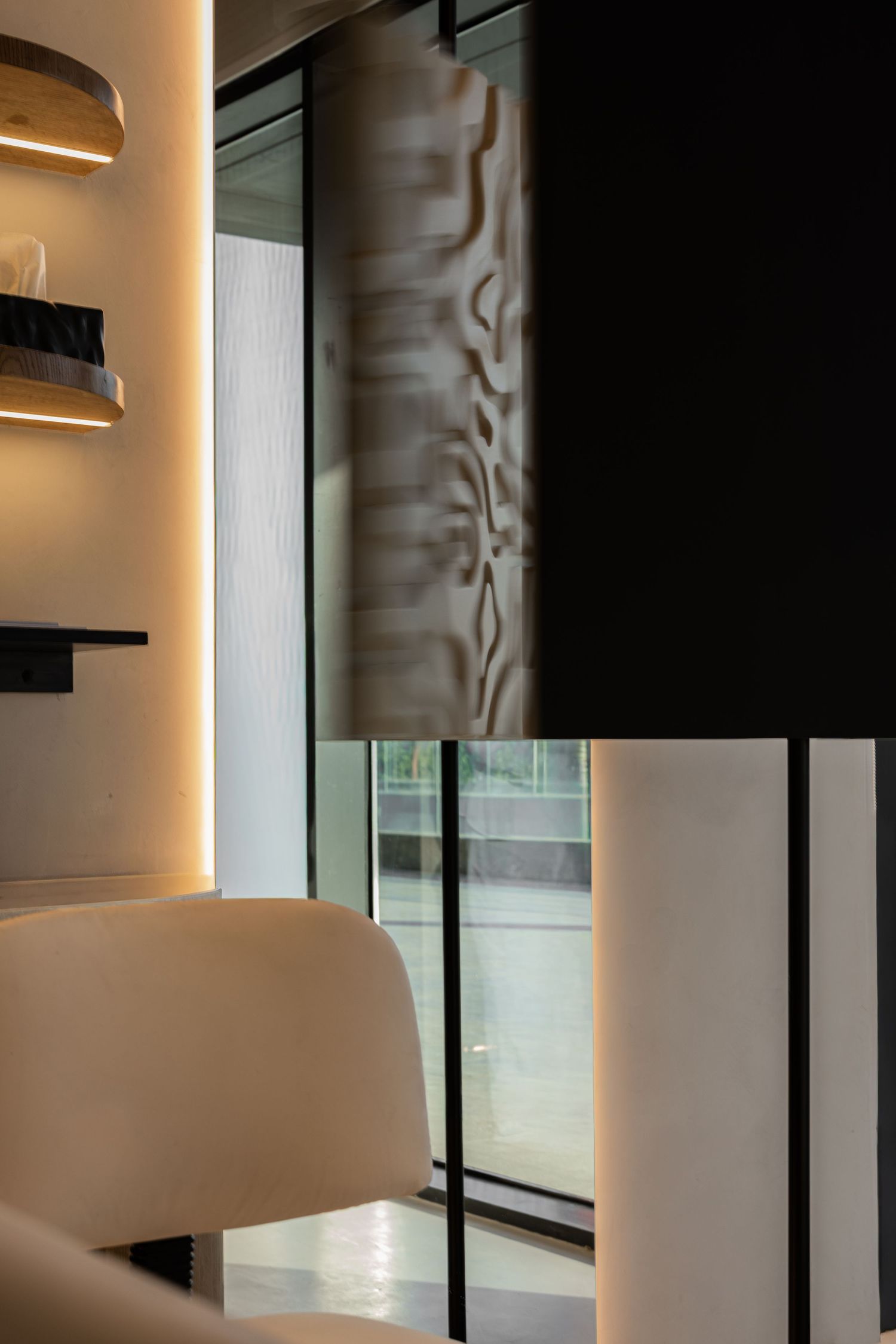 Modern interior with black glass partition, textured wall panel, and warm-lit shelving in a contemporary space.