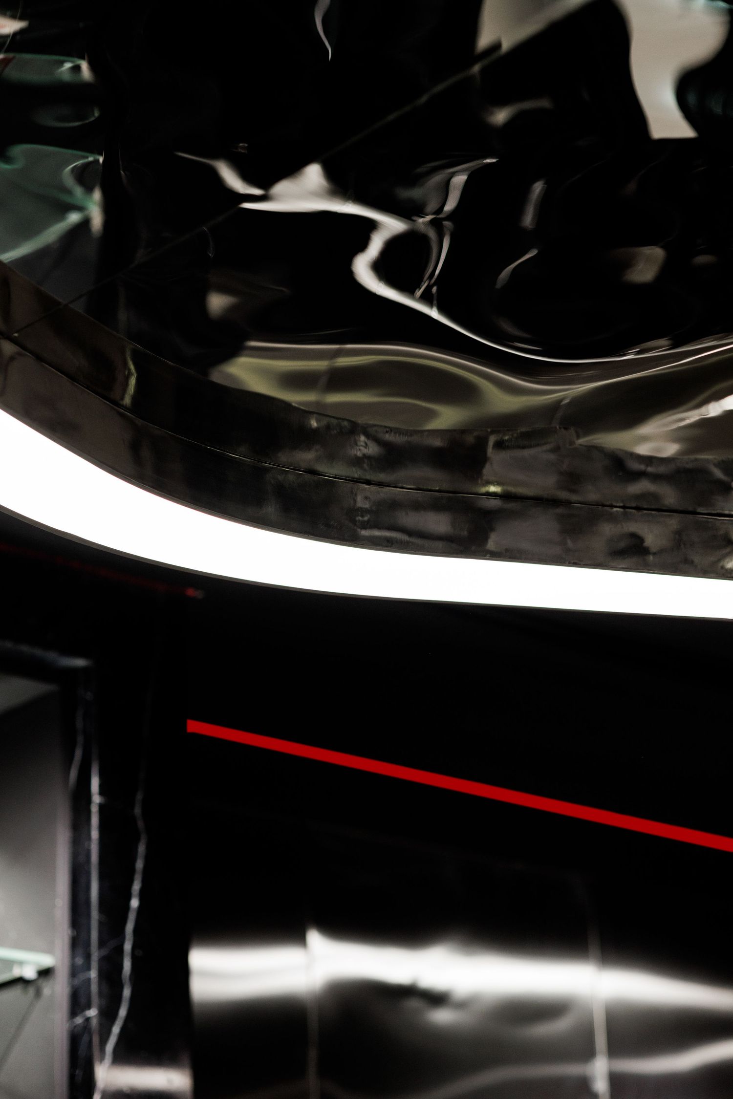 Close-up of glossy black rippled ceiling panel with curved white LED light and thin red accent stripe.
