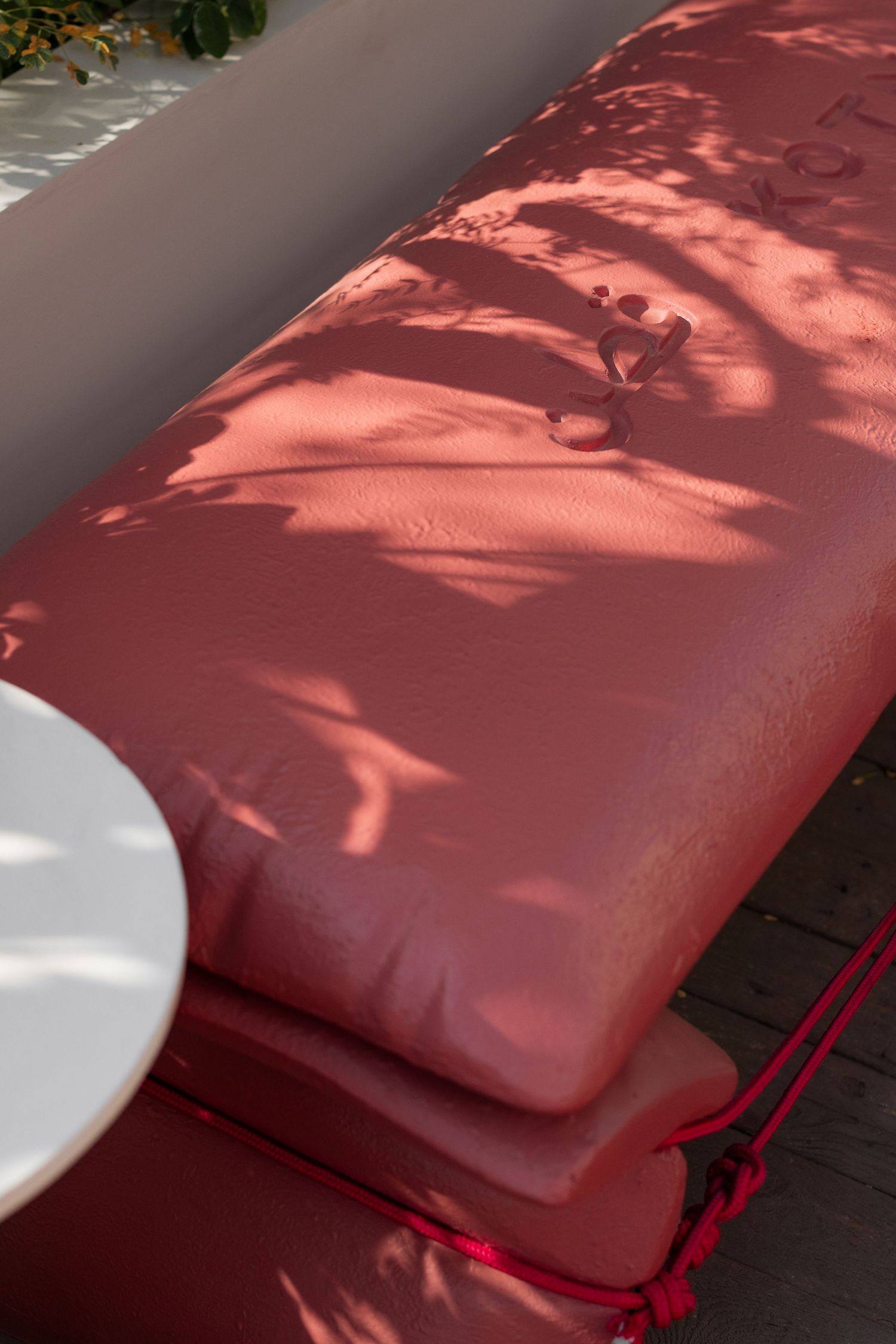 Close-up of terracotta red outdoor cushion with dappled tree shadow patterns in warm sunlight.
