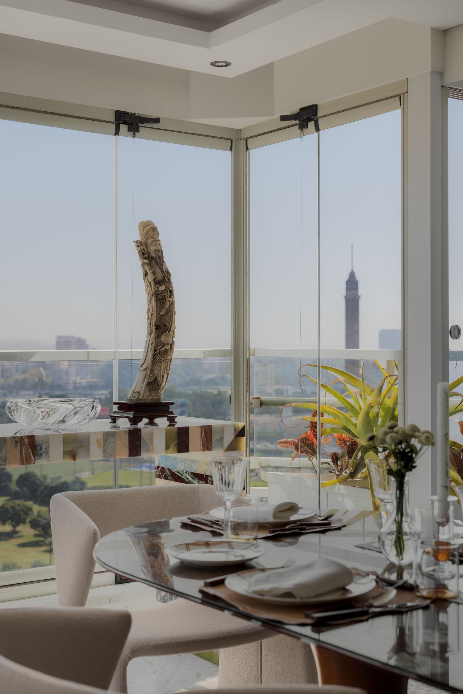 Elegant glass dining table set near floor-to-ceiling windows with panoramic city and Cairo Tower views.