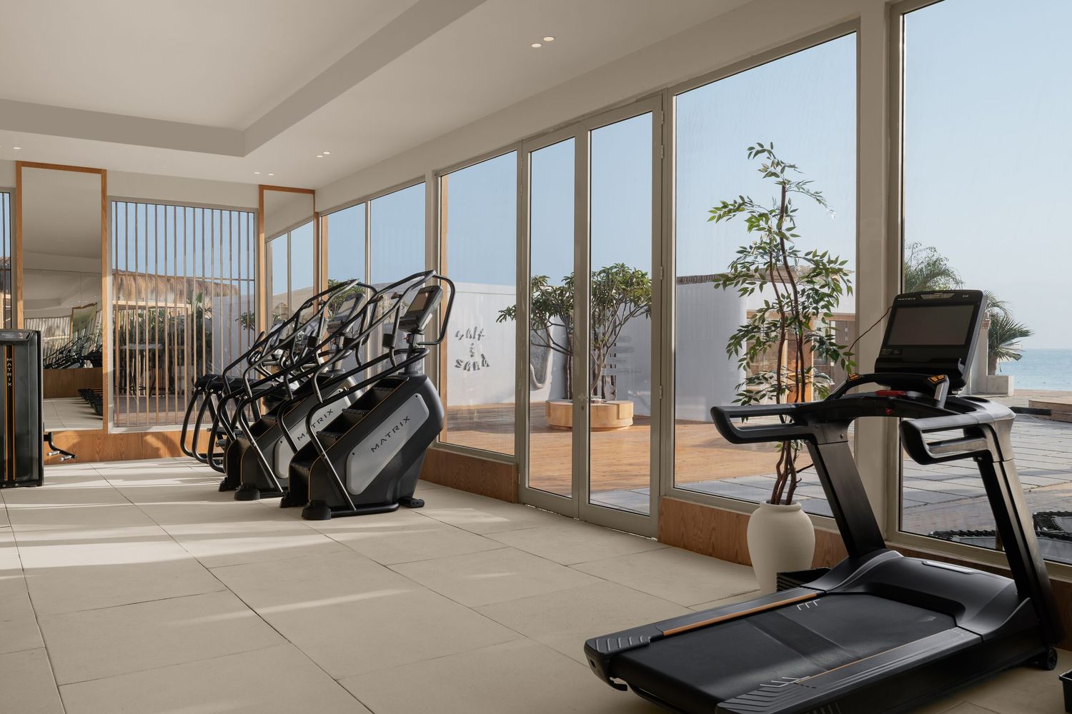 Bright modern gym with treadmills and cardio machines overlooking floor-to-ceiling windows with ocean and terrace views.
