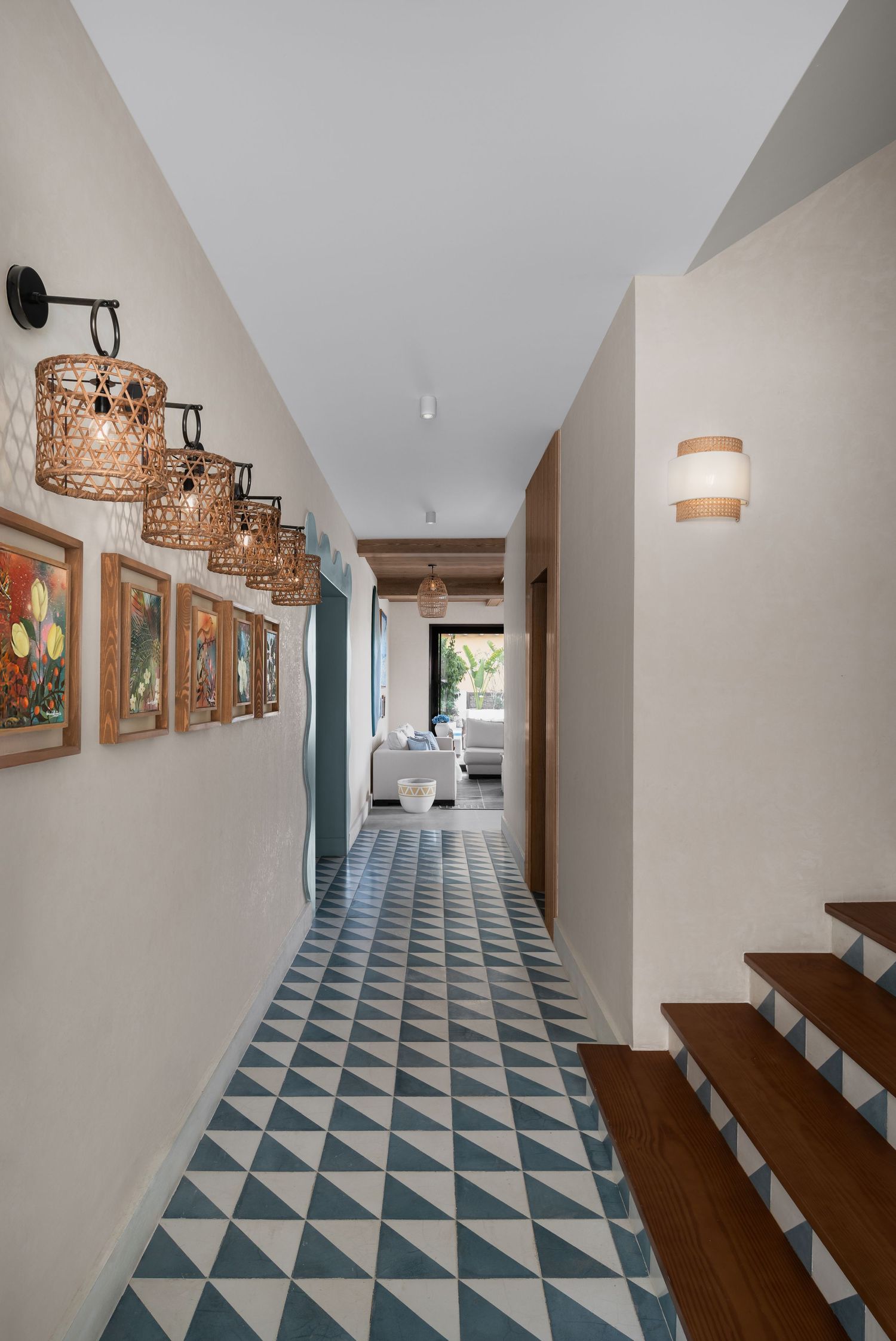 Bright hallway with geometric tile floor, rattan pendant lights, framed artwork, and wooden stairs.
