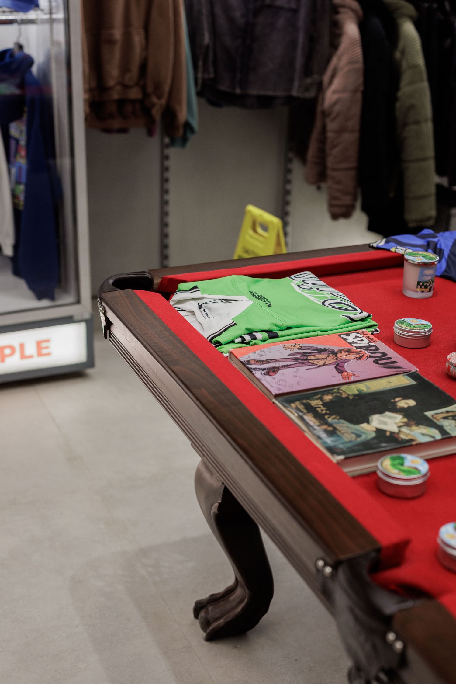 Pool table with red felt used as display for clothing, magazines, and accessories in a retail store.