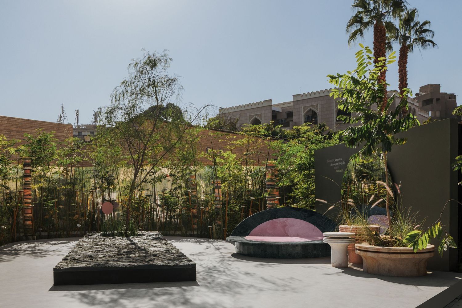 Serene outdoor courtyard with lush greenery, sculptural stone features, and pink dome accent in urban setting.