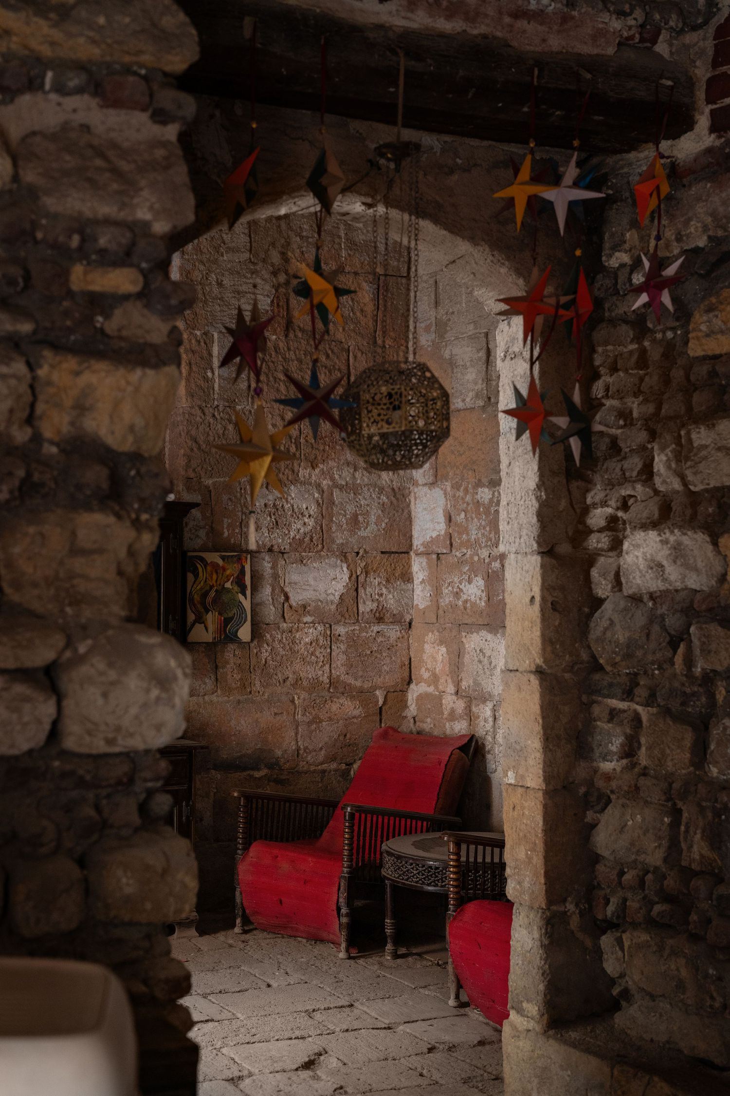Rustic stone alcove with colorful hanging star decorations and red upholstered vintage chairs inside.