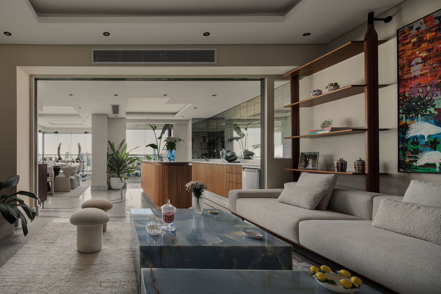 Bright open-plan living room with gray sectional sofa, glass coffee table, shelving unit, and large colorful abstract painting.