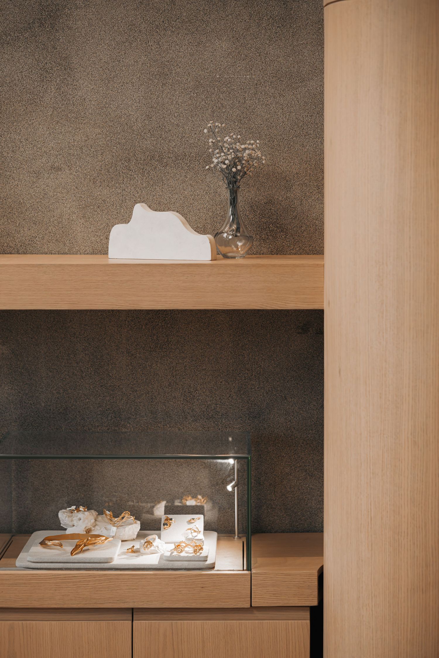 Elegant wood shelving display with glass jewelry case, white decorative object, and small dried flower arrangement.