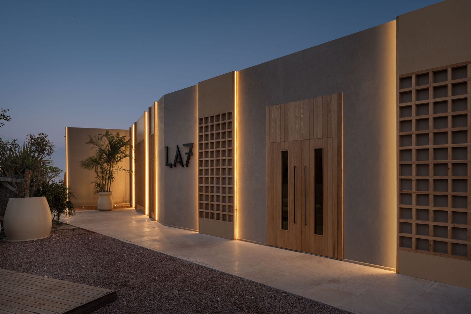 LA7 luxury property entrance with warm LED uplighting, decorative block wall panels, and elegant wooden doors at dusk.