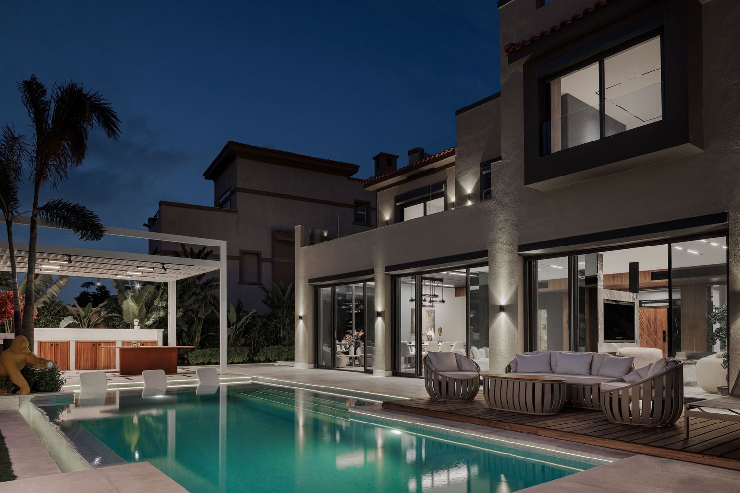 Modern luxury villa exterior at night with illuminated pool, outdoor seating, and floor-to-ceiling glass walls.