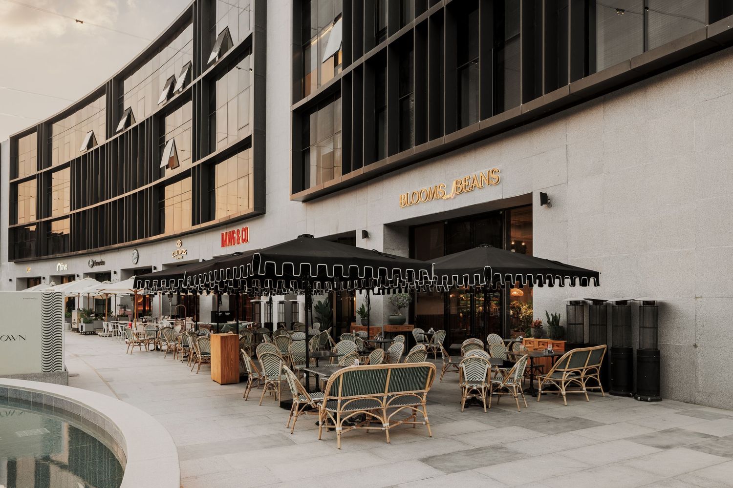 Upscale outdoor restaurant terrace with black umbrellas and wicker chairs at a modern commercial complex.