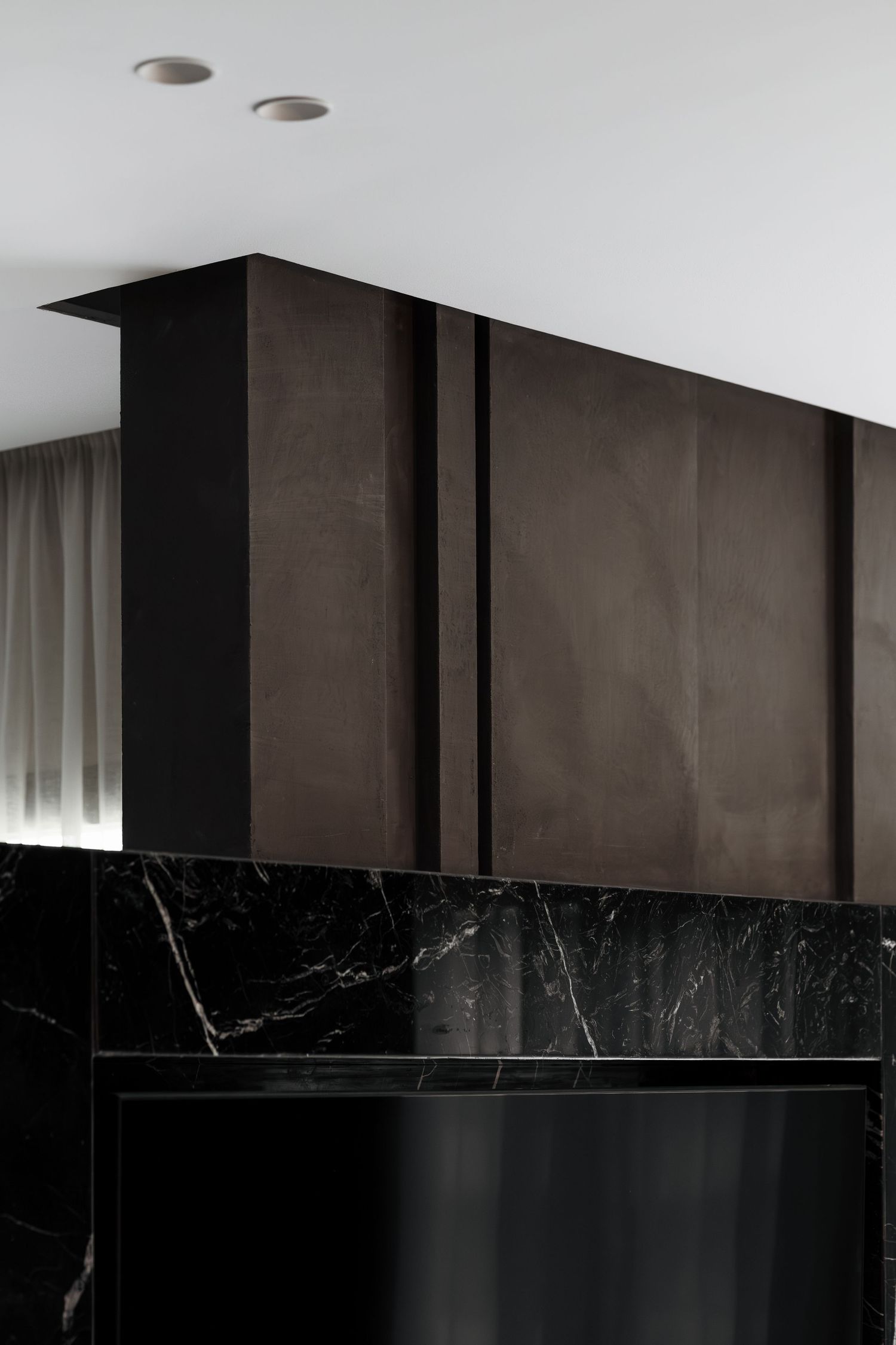 Dark bronze ceiling cabinet above black marble fireplace surround in a contemporary luxury living room.