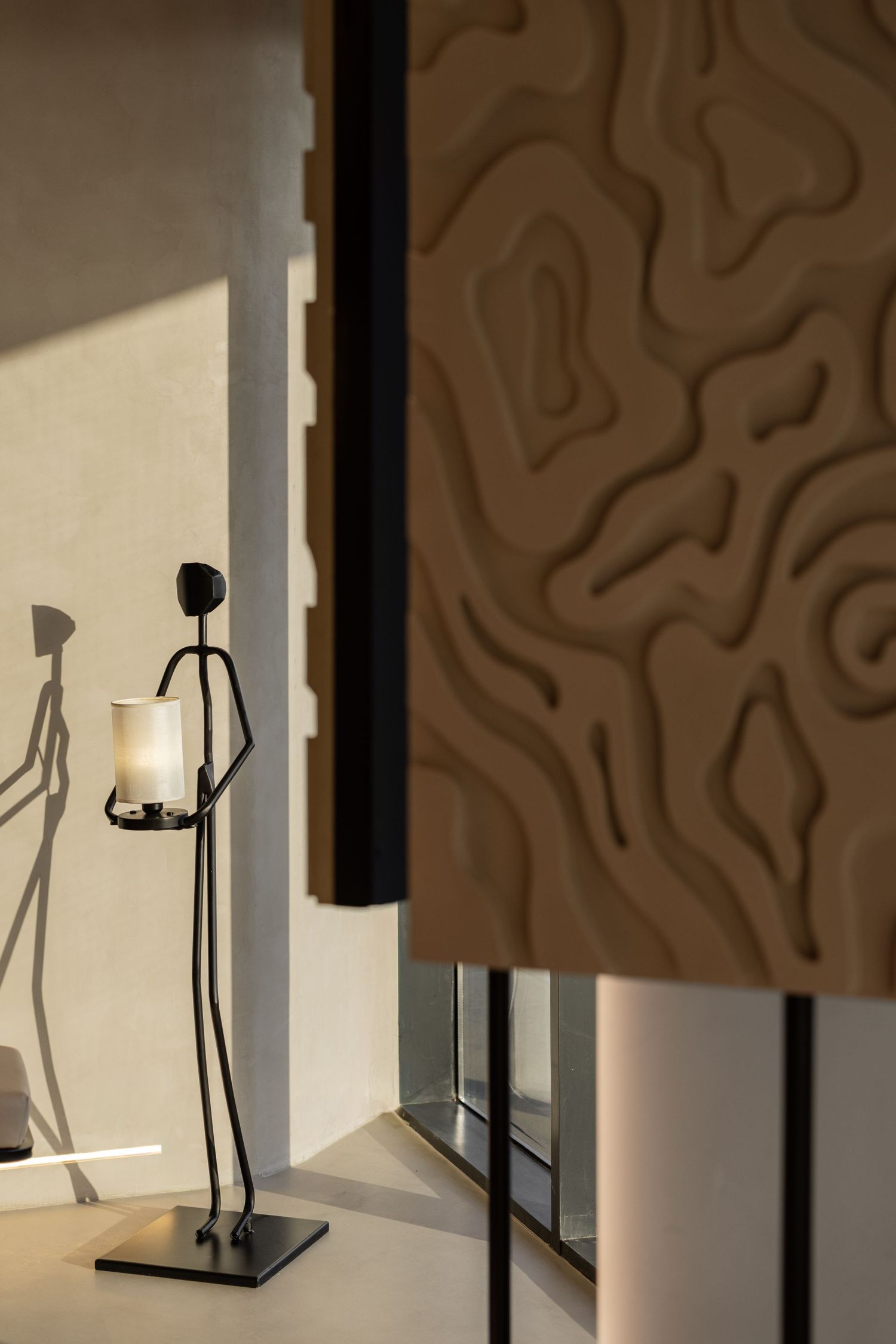 Modern interior corner with sculptural brown textured wall panel and elegant black figurine candle holder.
