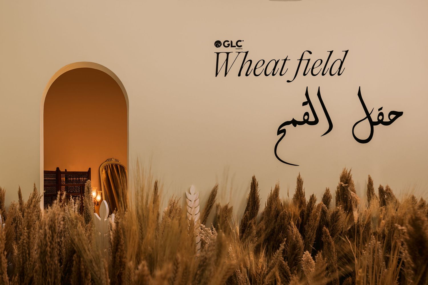 Woman standing in arched doorway surrounded by wheat field with GLC Wheat Field Arabic branding.
