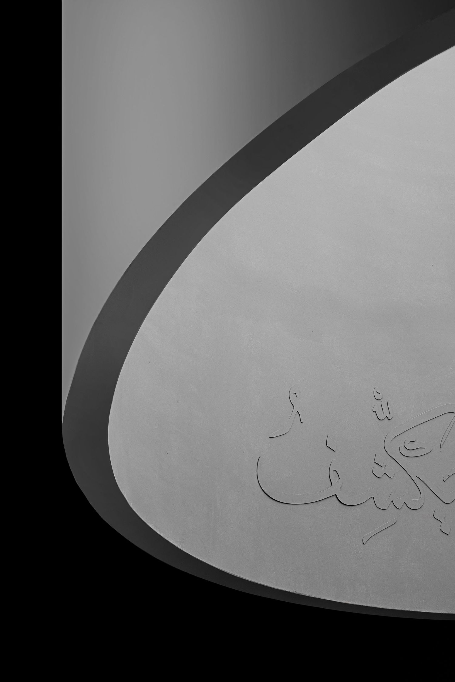 Black and white close-up of curved architectural surface with Arabic calligraphy engraving.