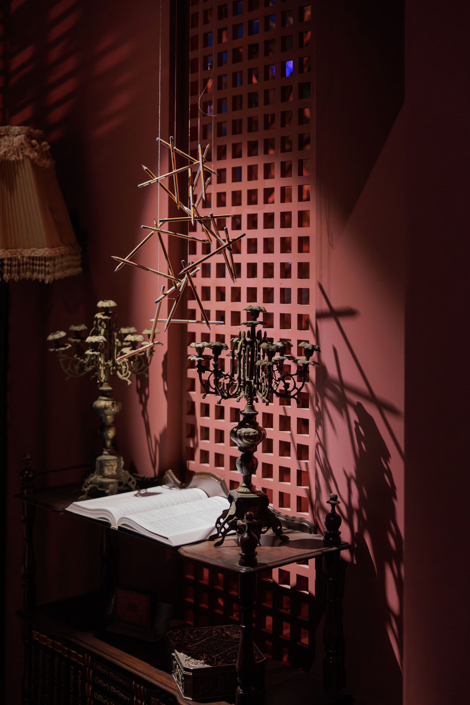 Antique wooden desk with candelabra, lamp, and bare branch decoration against a pink lattice wall.