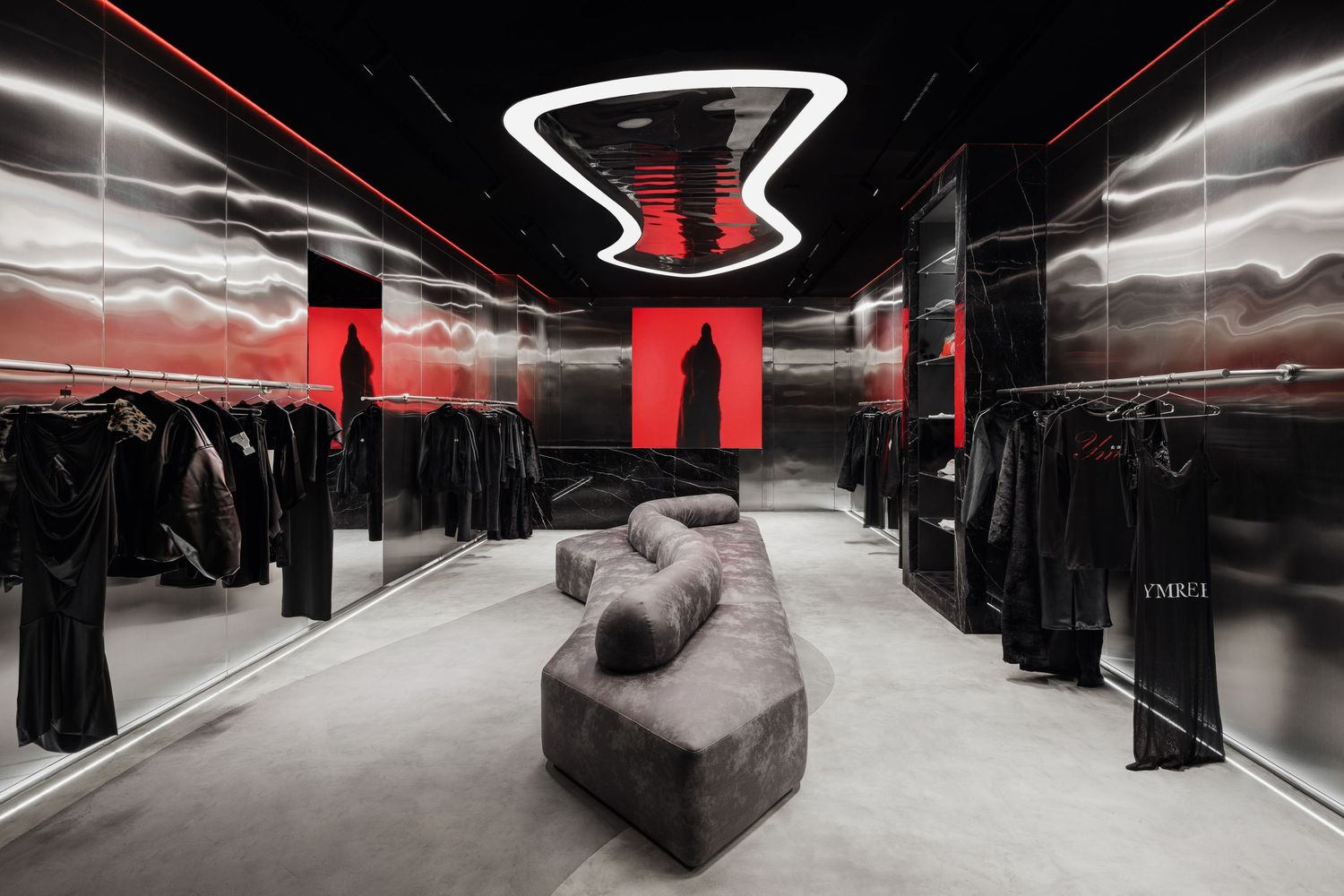 Sleek fashion store interior featuring black reflective walls, red accent lighting, gray curved sofa, and clothing racks.