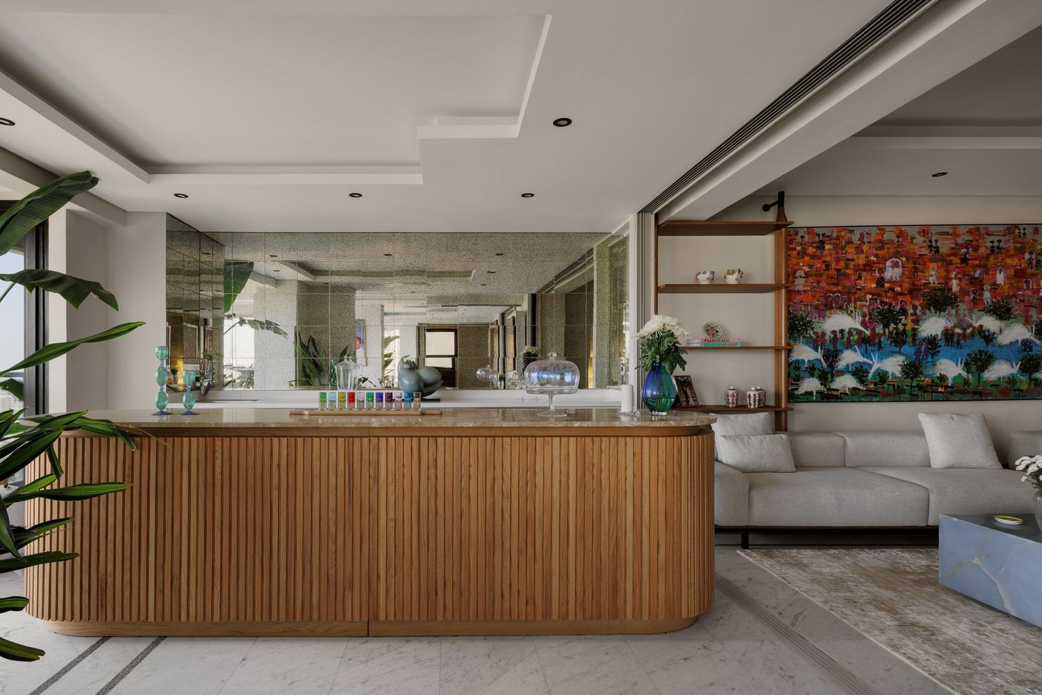 Modern open-plan interior featuring a wooden ribbed kitchen island, mirror backsplash, and gray sectional sofa with artwork.