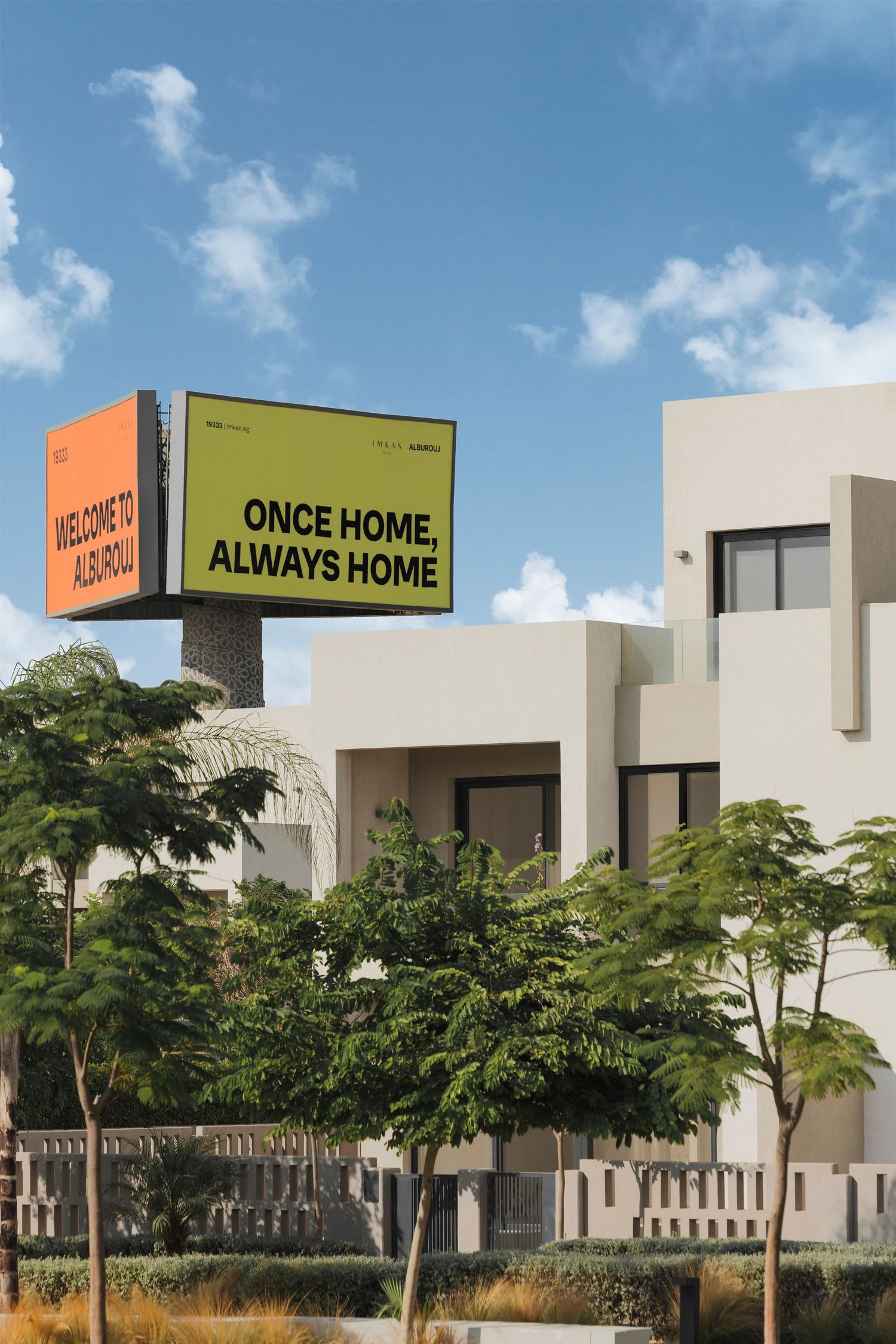 Billboard reading 'Once Home, Always Home' above modern white residential villas with palm trees under blue sky.