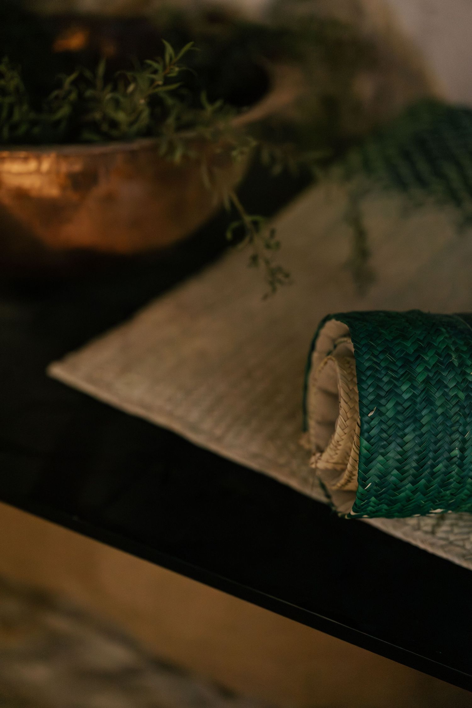 Rolled green woven mat on a textured surface beside a copper bowl with greenery.