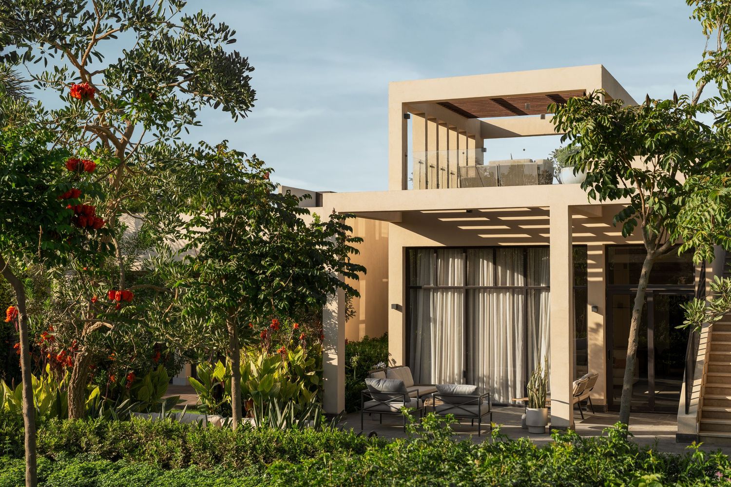 Elegant modern villa surrounded by lush tropical gardens with colorful flowering plants and natural stone pathways.