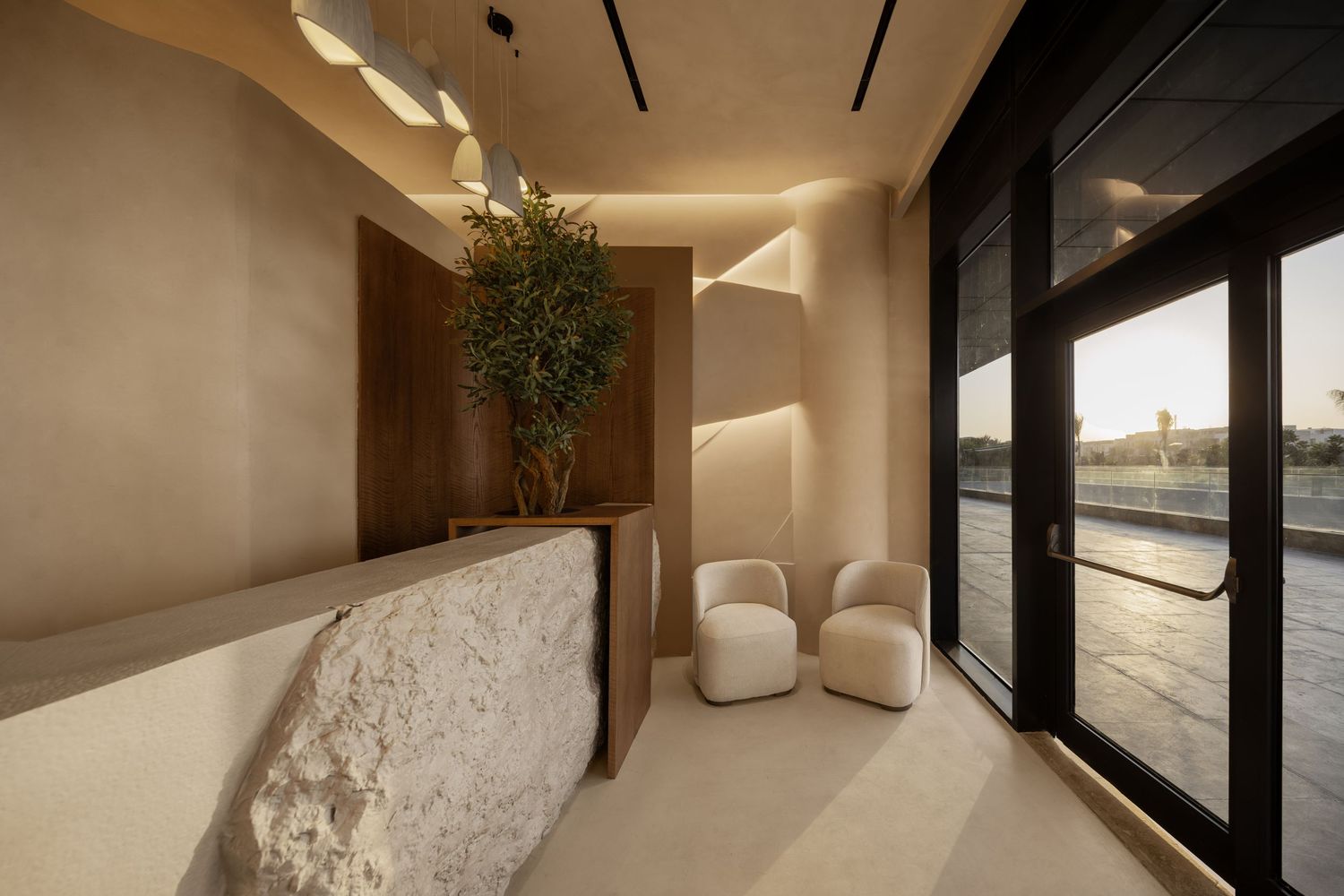 Modern minimalist reception area with marble desk, white chairs, and olive tree by floor-to-ceiling windows.