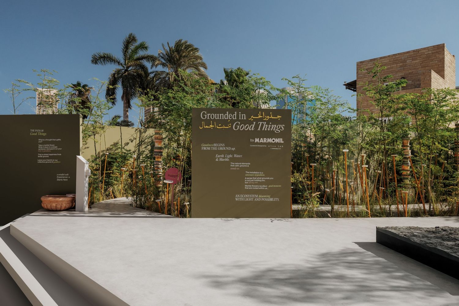 Outdoor exhibition signage reading Grounded in Good Things surrounded by bamboo and palm trees.