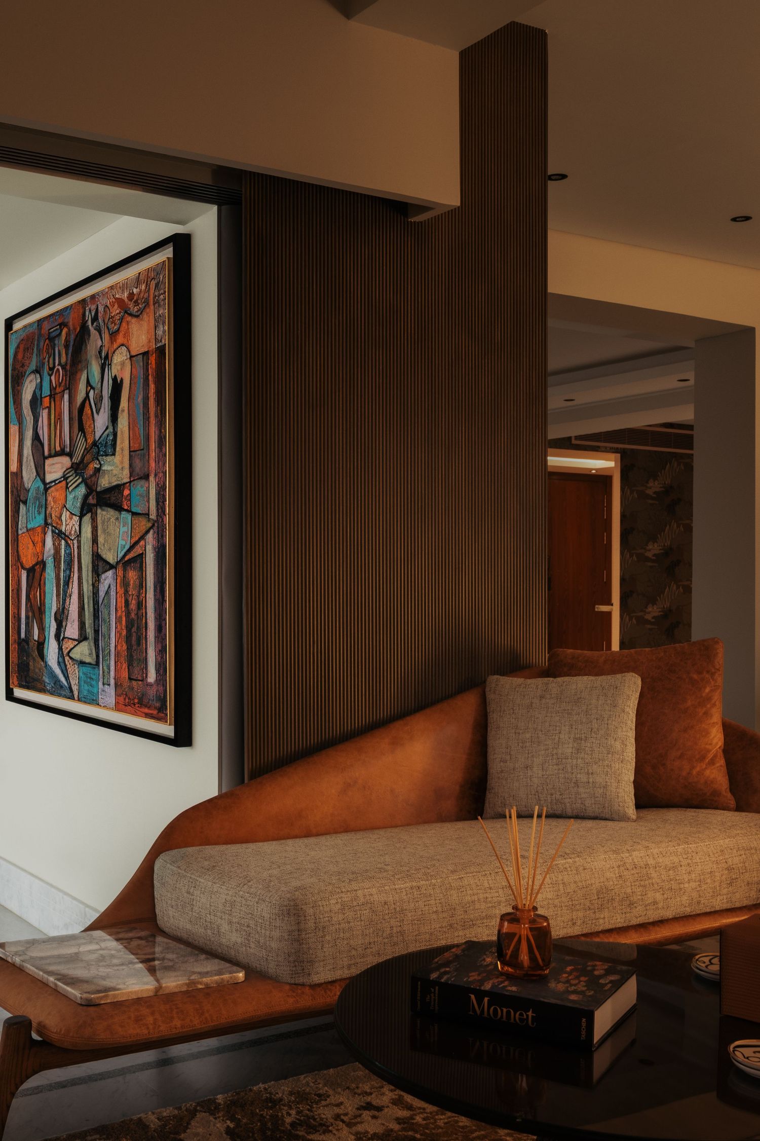 Stylish interior with curved leather wooden sofa, abstract cubist artwork, dark wood panel, and reed diffuser on table.