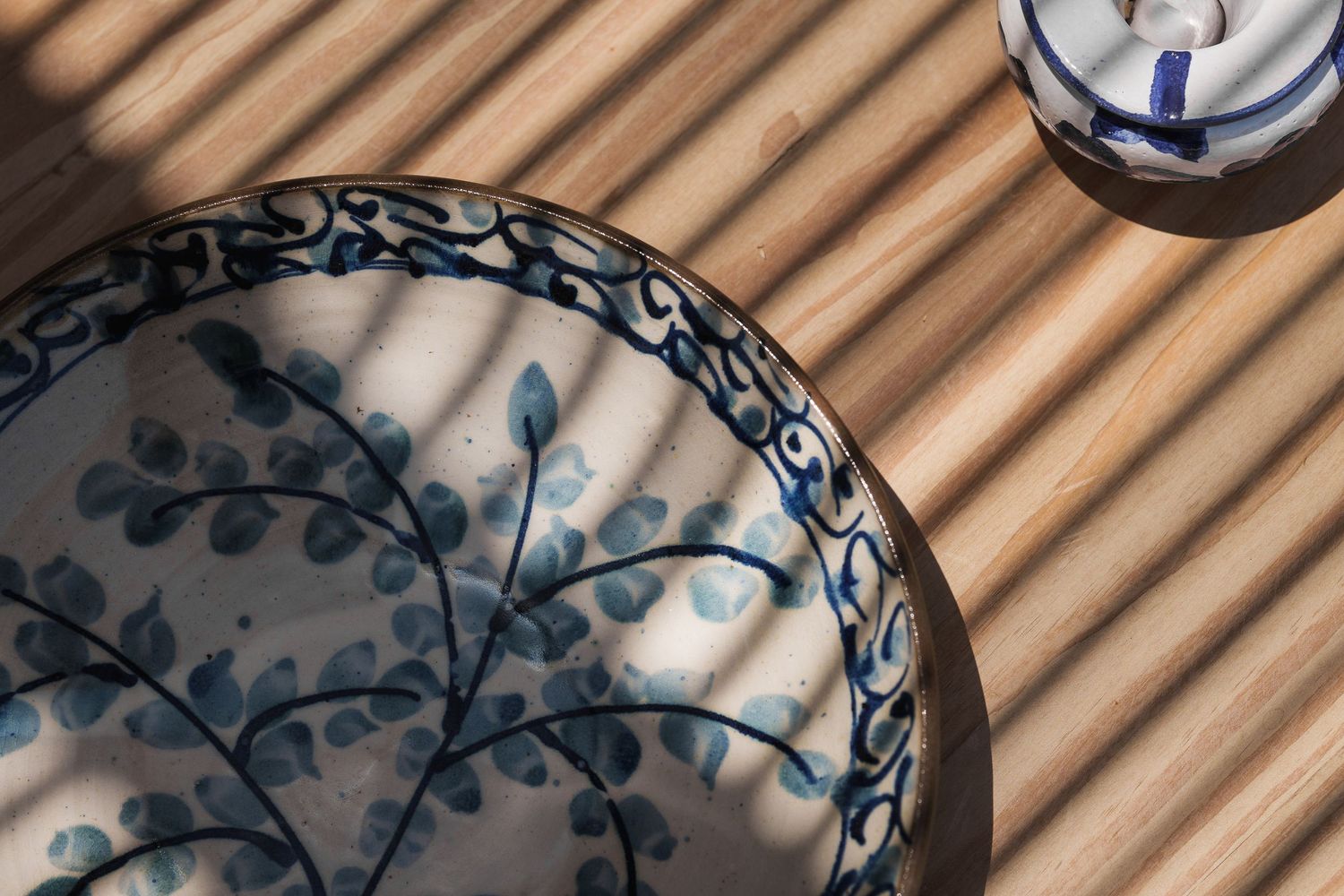 Blue and white floral ceramic plate with intricate botanical pattern on wooden surface with soft shadows.