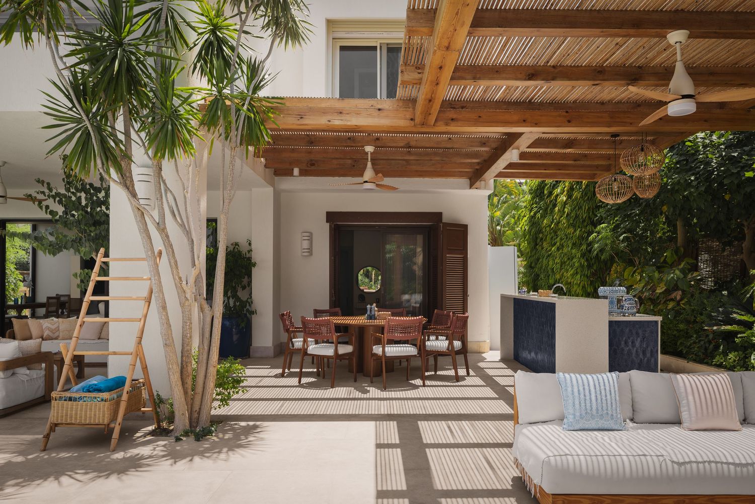 Spacious outdoor patio featuring pergola, dining area, lounge seating, and lush tropical landscaping.