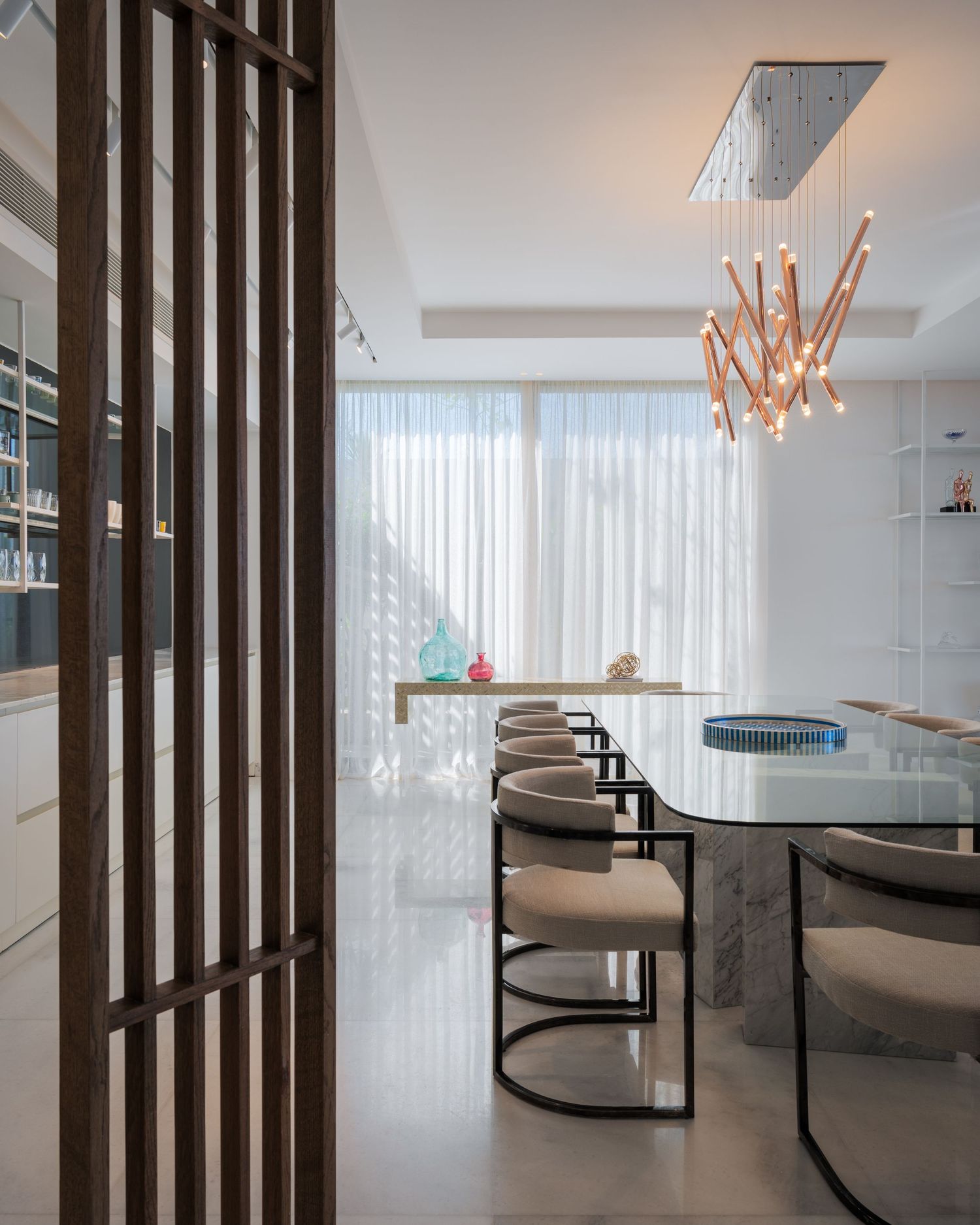 Sophisticated dining room with marble table, curved chairs, wood slat divider, and rose gold chandelier.