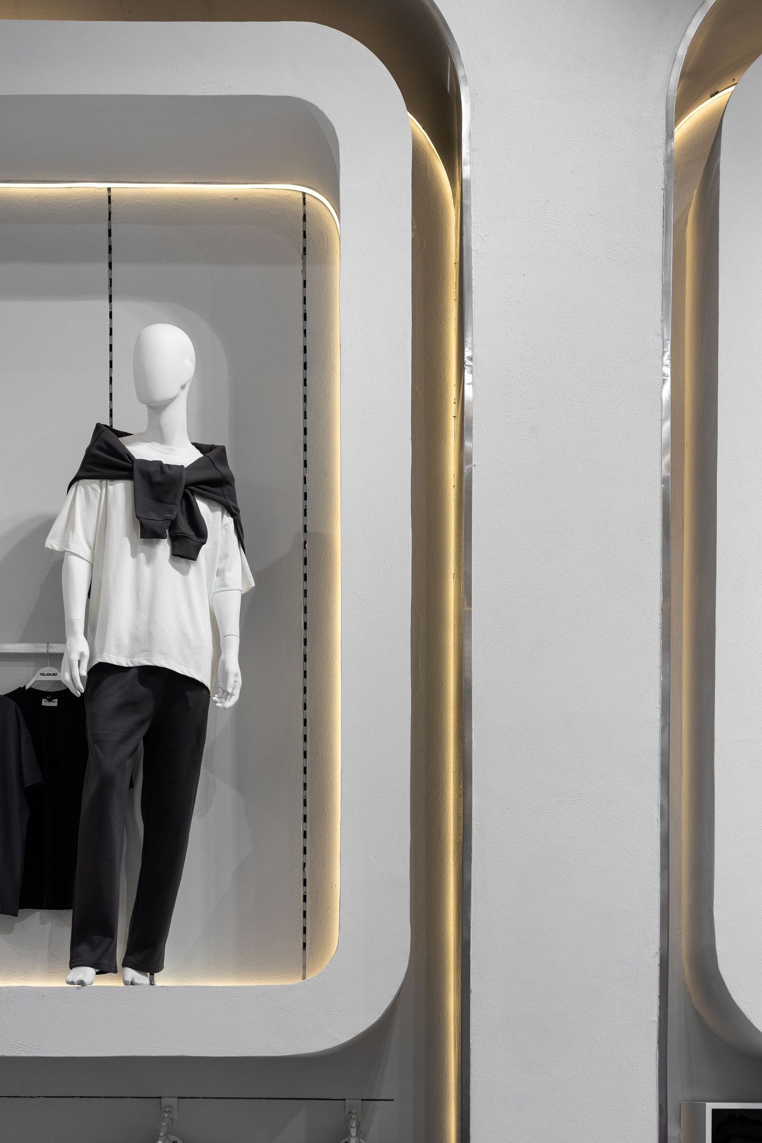 Minimalist boutique display featuring white mannequin in monochrome outfit within illuminated arched niche with warm LED lighting.