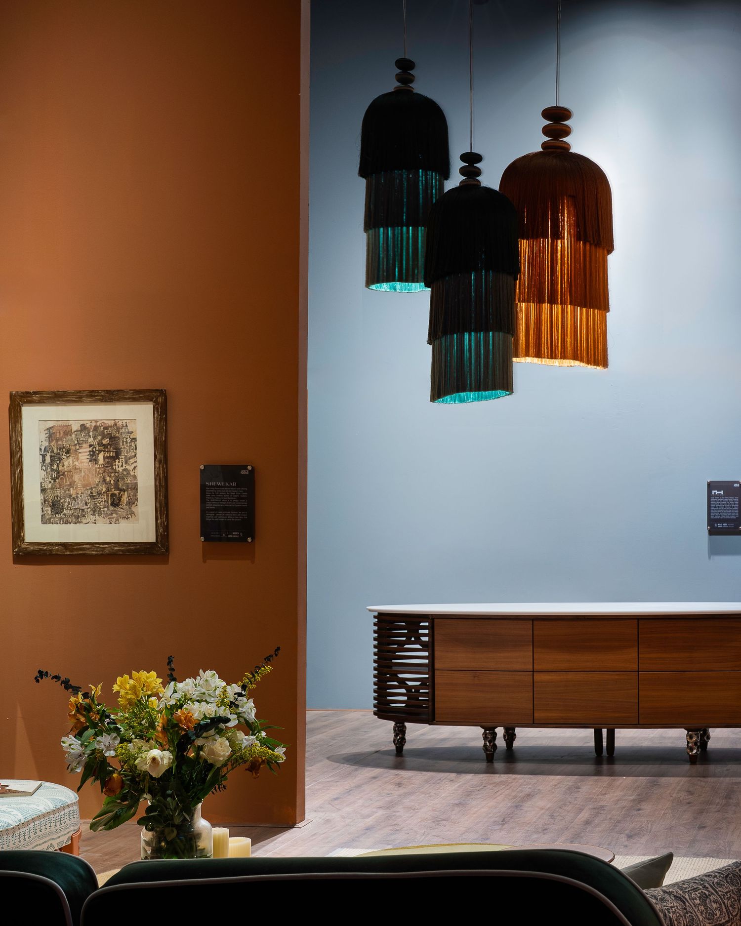 Elegant interior with teal and copper fringe pendant lights above walnut sideboard with fresh flowers.